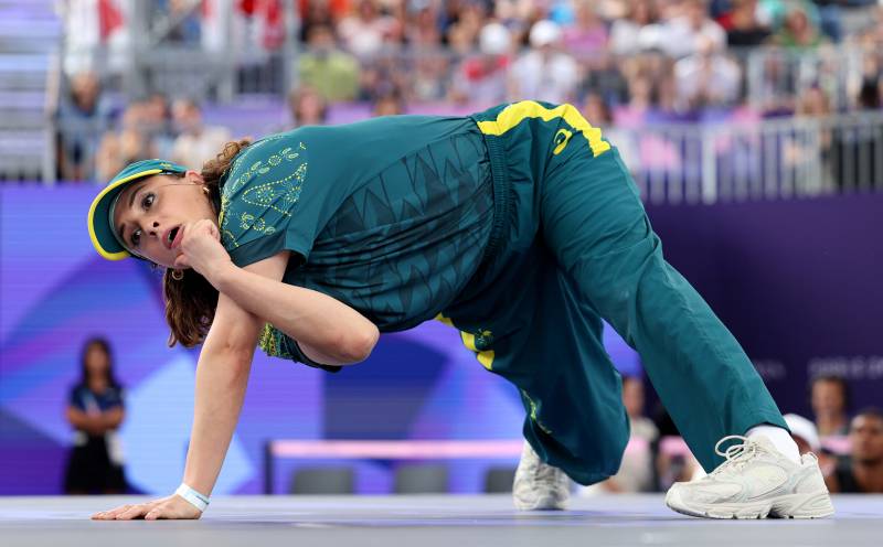 A white woman in green tracksuit contorts herself on the floor in front of a packed stadium.