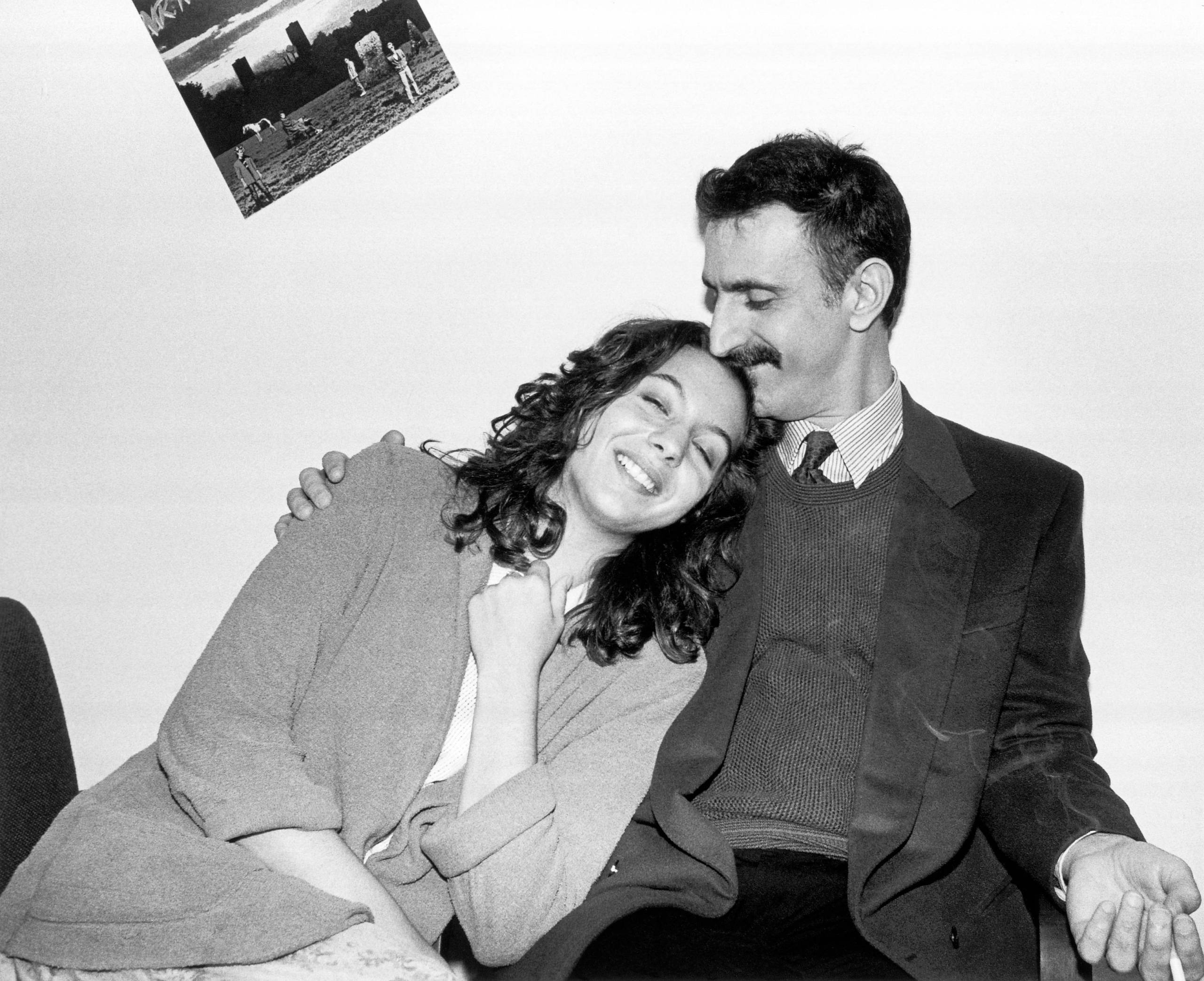A 1970s-era photo of a man in a suit with a mustache embracing a younger woman, also wearing a suit.