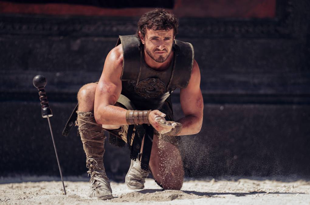 Man crouches in gladiator outfit and rubs sand between hands