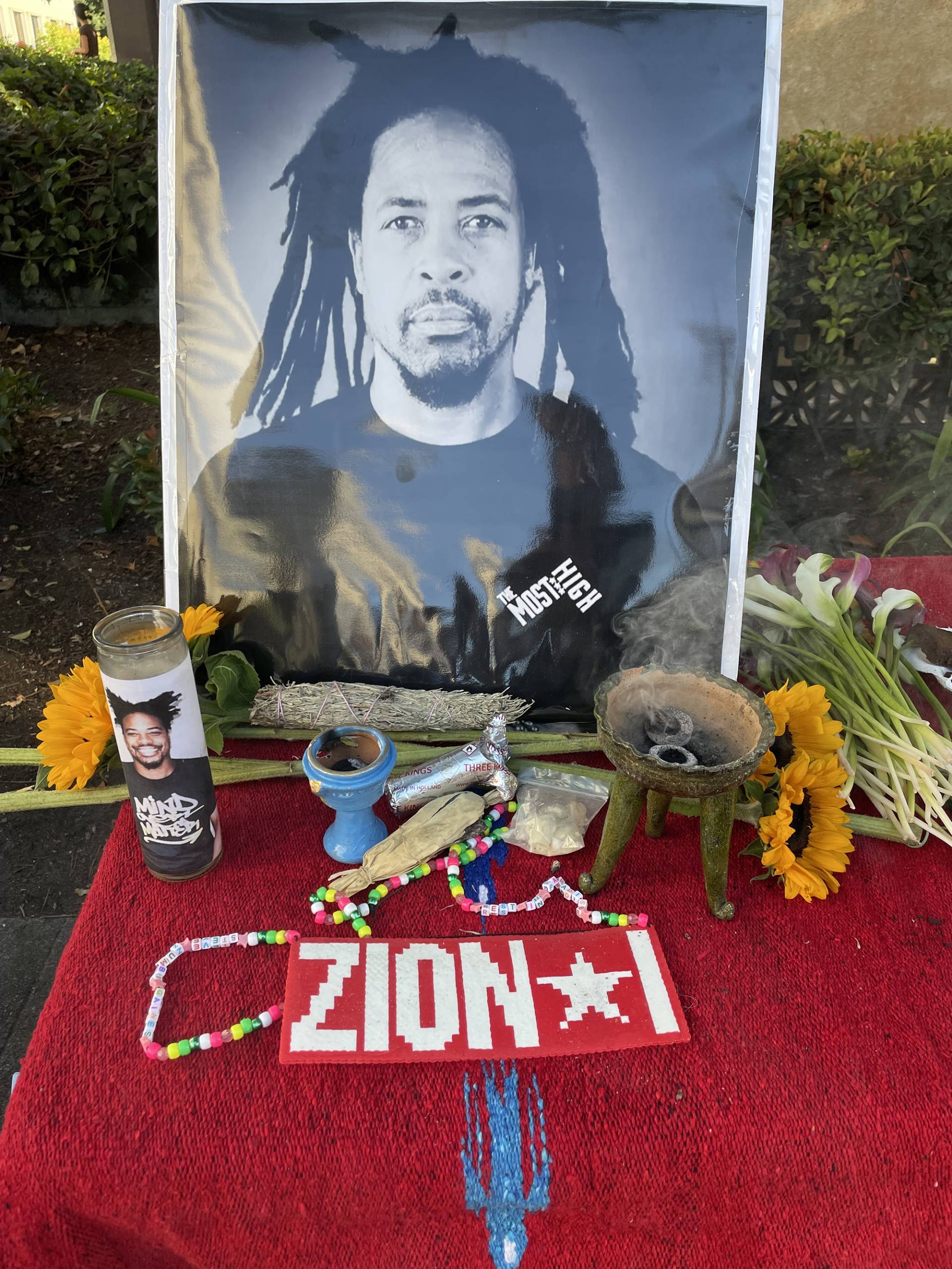 An altar bears a large portrait of Zumbi, the name of his group Zion I, flowers and candles. 