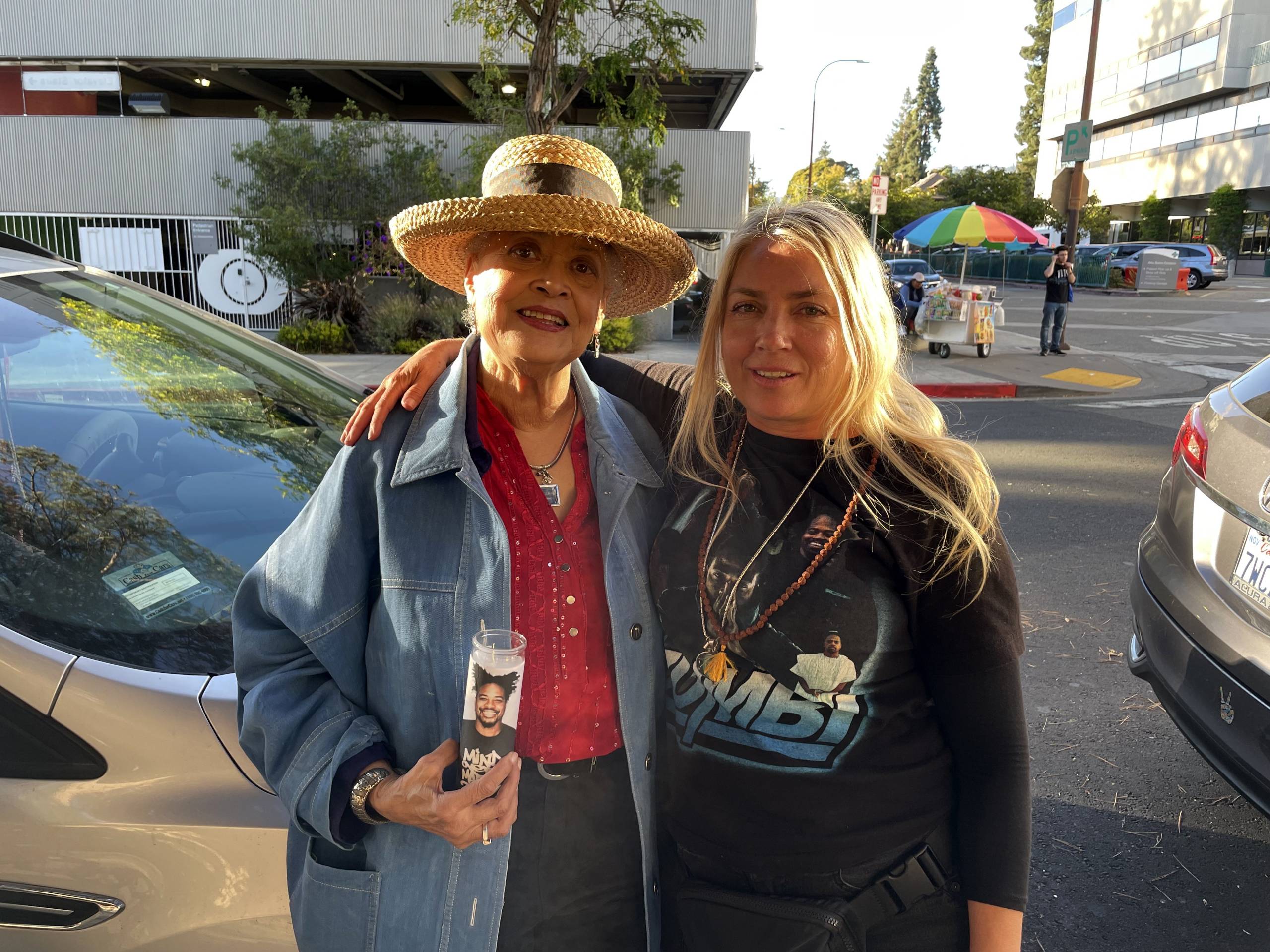 Two women hug. One wears a T-shirt with Zumbi's portrait while the other holds a candle with his picture on it. 