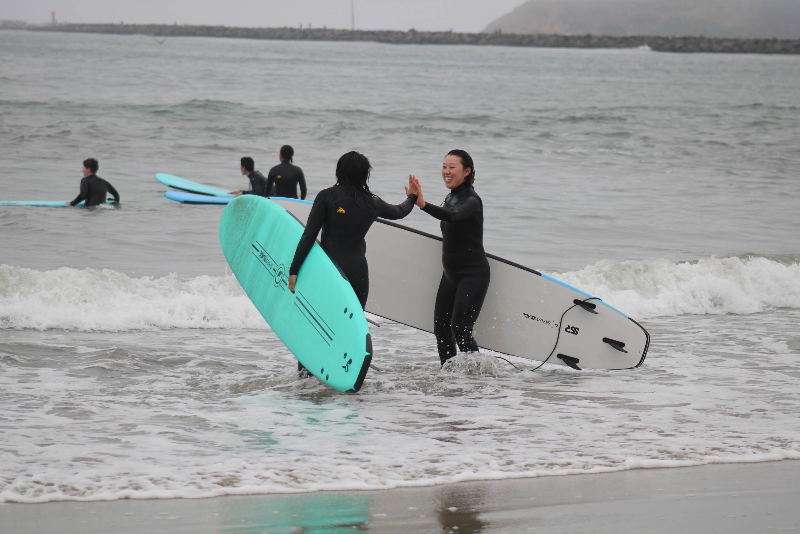 Two surfers high five in the water.