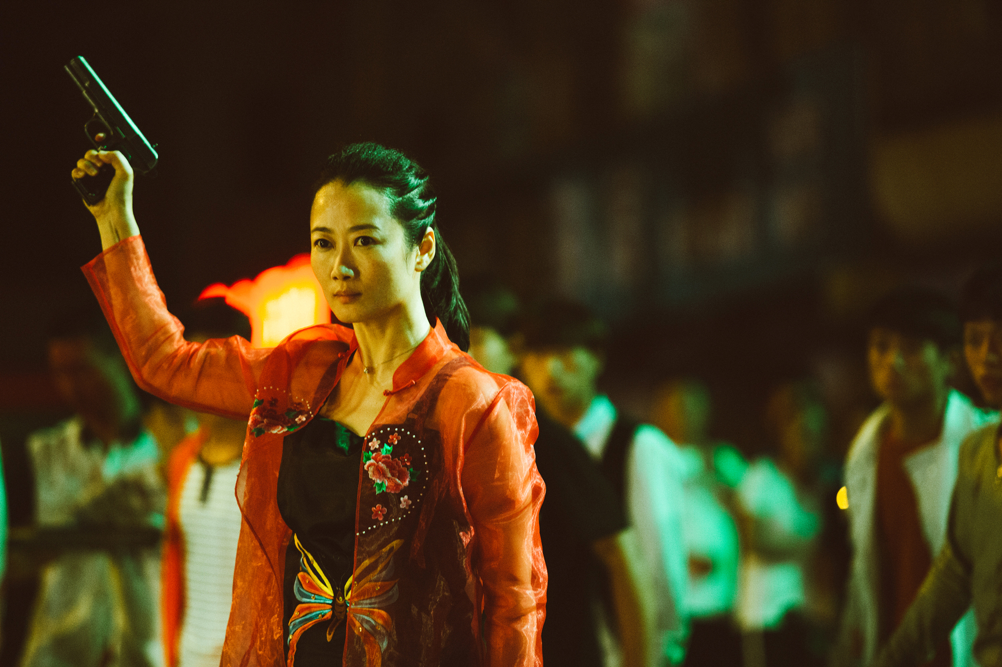 woman stands in front of crowd with a gun raised to sky in right hand