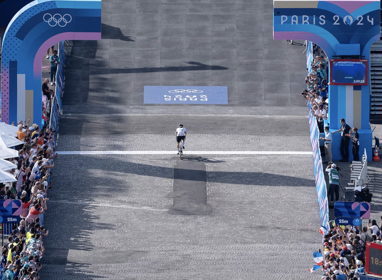 A cycling finish line filmed from above. A lone female cyclist crosses without any other competitors in sight.