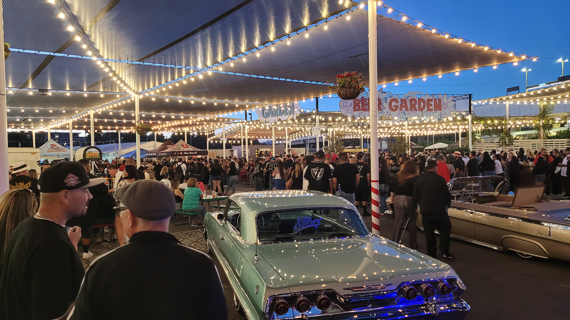 View of an outdoor beer garden with vintage lowrider cars on display.