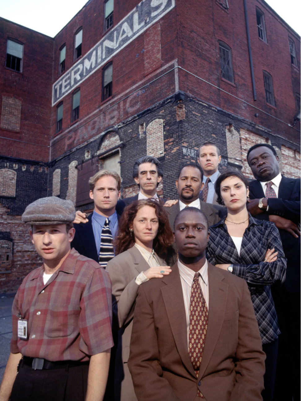 Standing in front of an old red brick building are seven men of various ages and races and two white women. Almost everyone is wearing a suit.