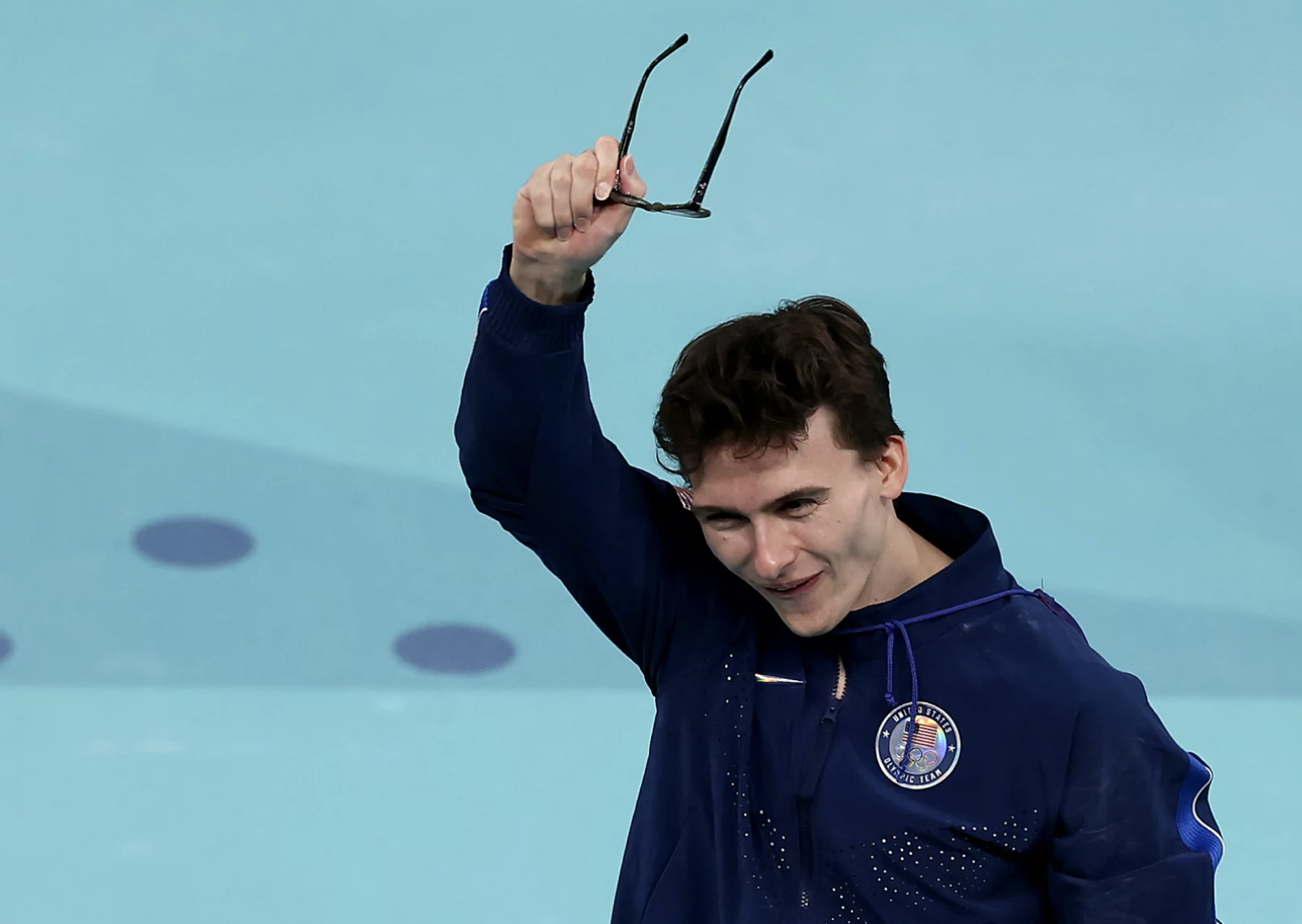 A man wearing a track jacket waves a pair of spectacles over his head.