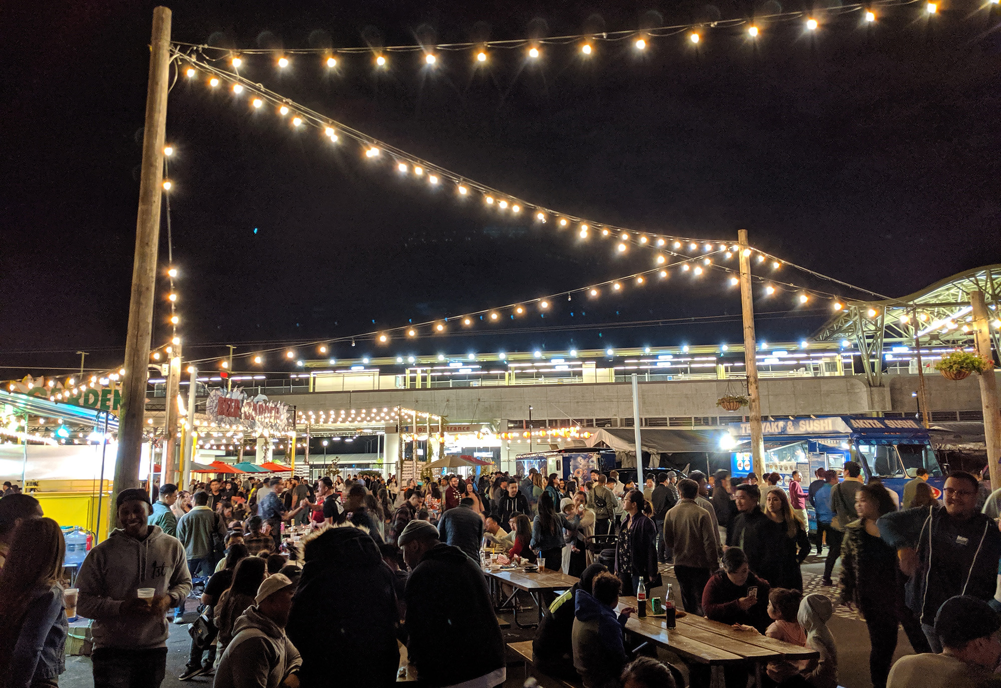 A crowded night market lit up with string lights.