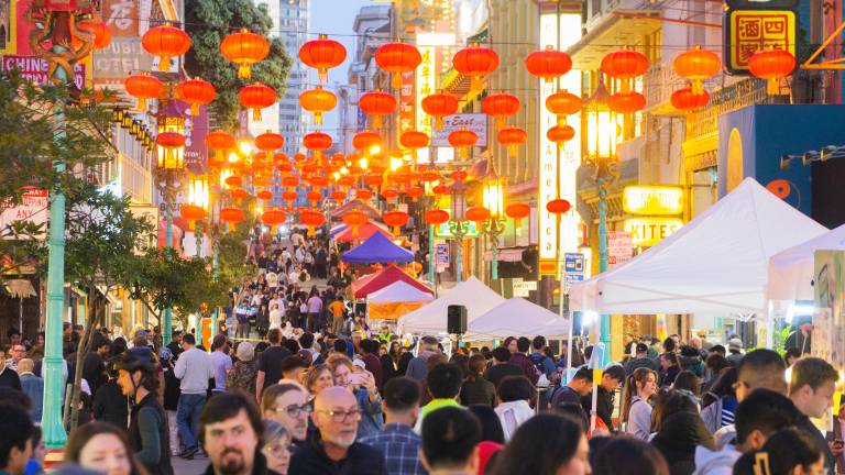 Crowded Chinatown street with red lanterns strung up above.