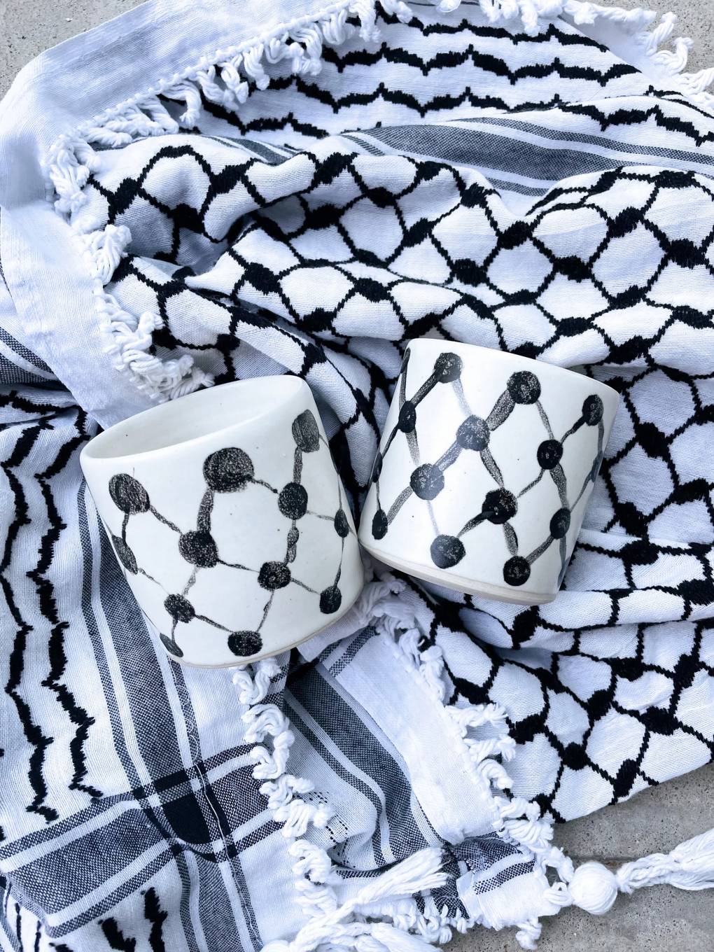 Coffee cups with a black-and-white checked pattern, placed on top of a keffiyeh scarf with a similar design.