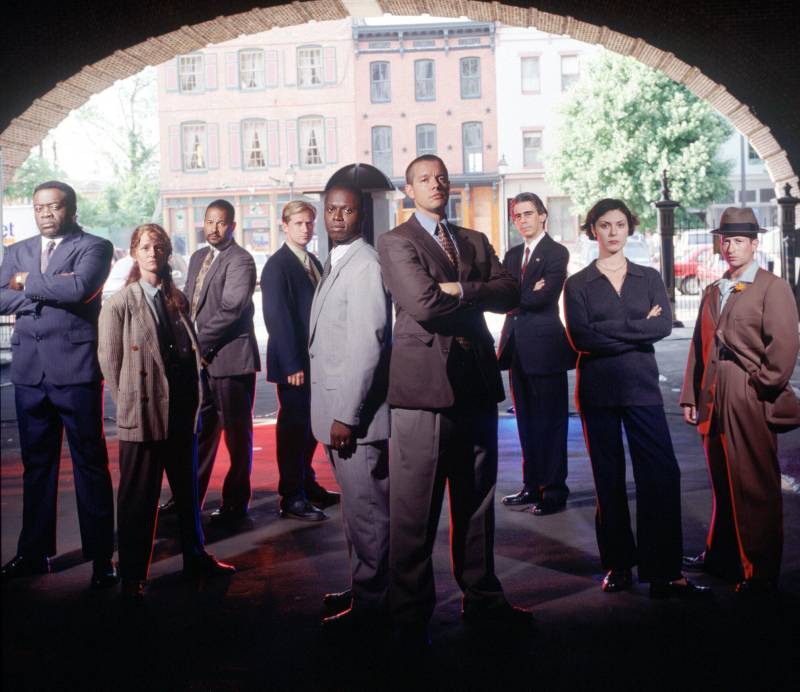 Seven men and two women stand at the edge of a tunnel. All are wearing suits and serious expressions.