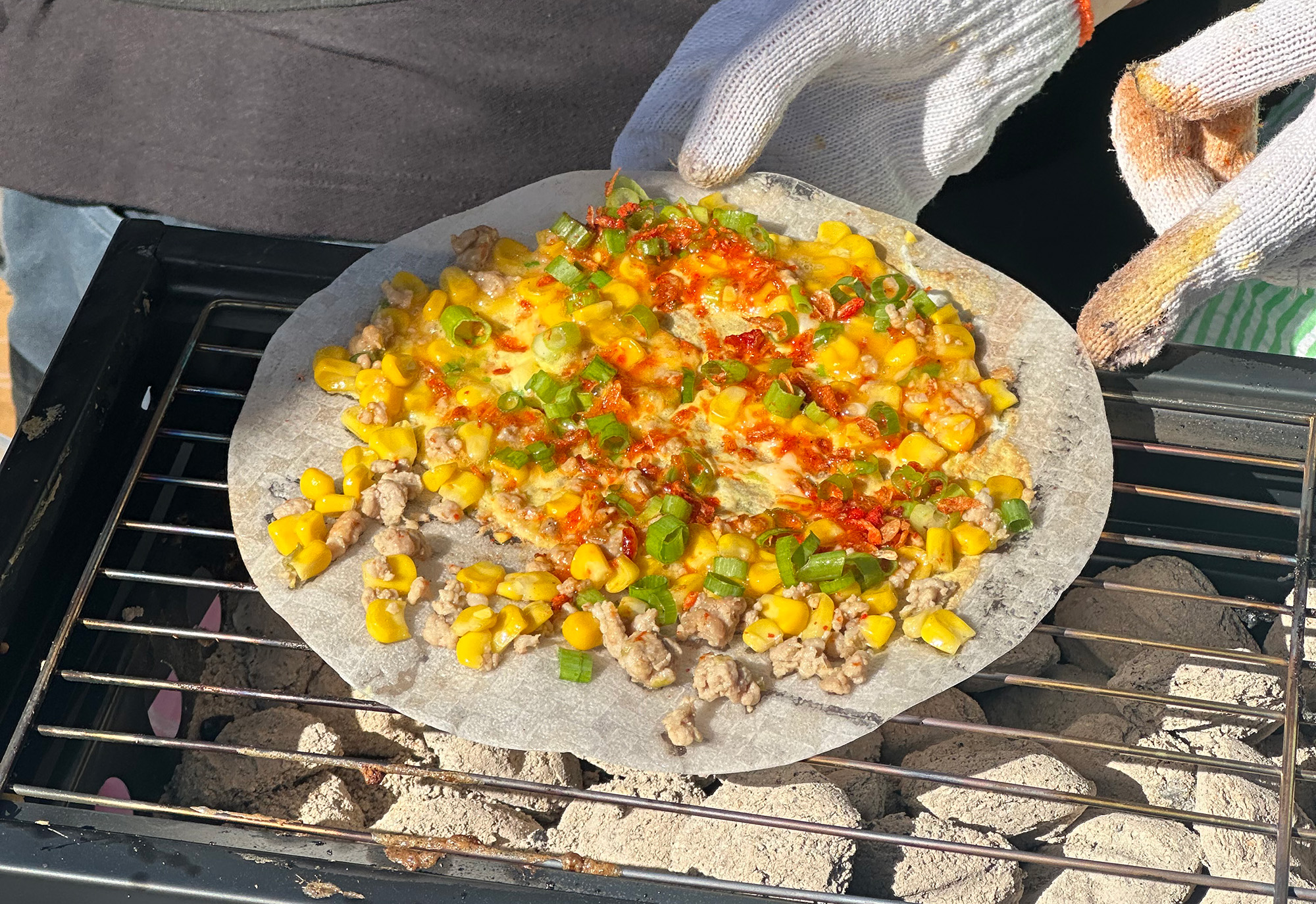 Rice paper topped with corn and ground meat being grilled over hot charcoal.