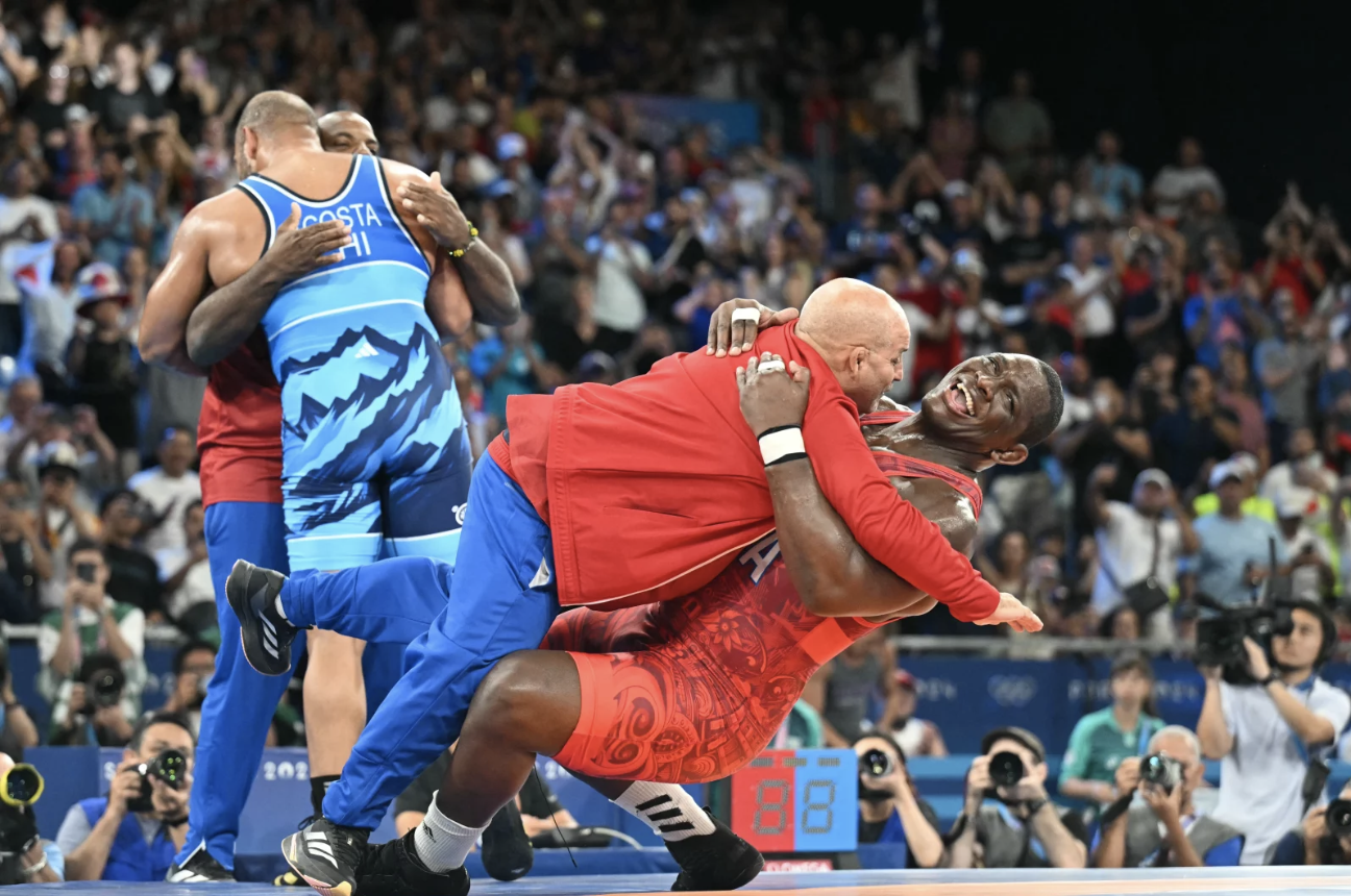 A gleeful looking wrestler falls to the ground dragging his coach with him.