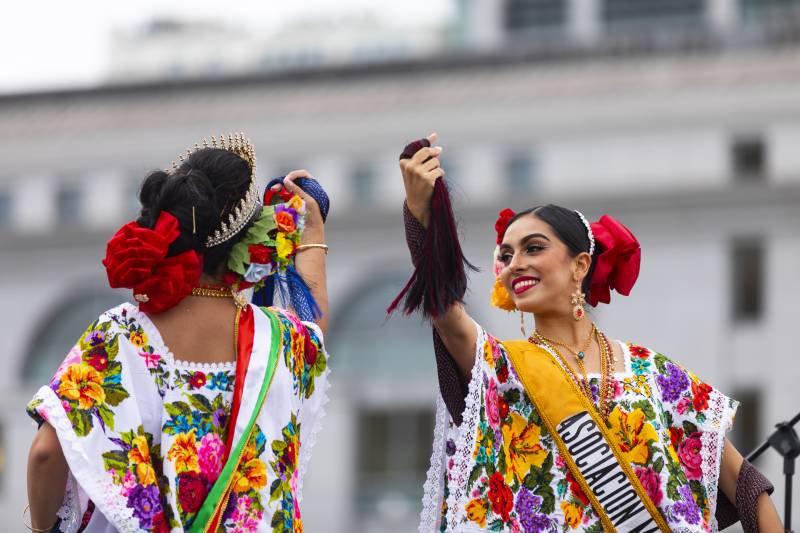 two dancers in colorful traditional costumes with sashes across chests