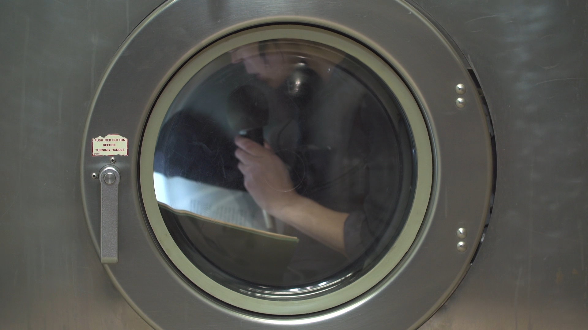 person inside of circular clothing washer door holding mic and looking at paper