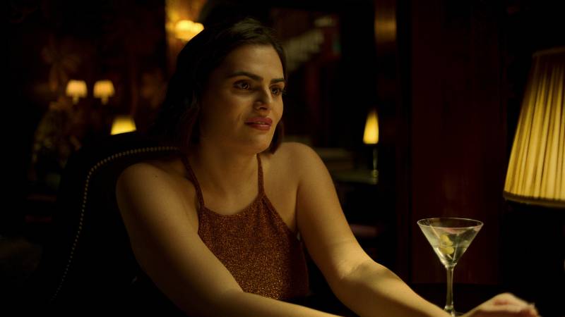 A still from the show 'Baby Reindeer' where actress Nava Mau is seated at a dimly lit cocktail bar.