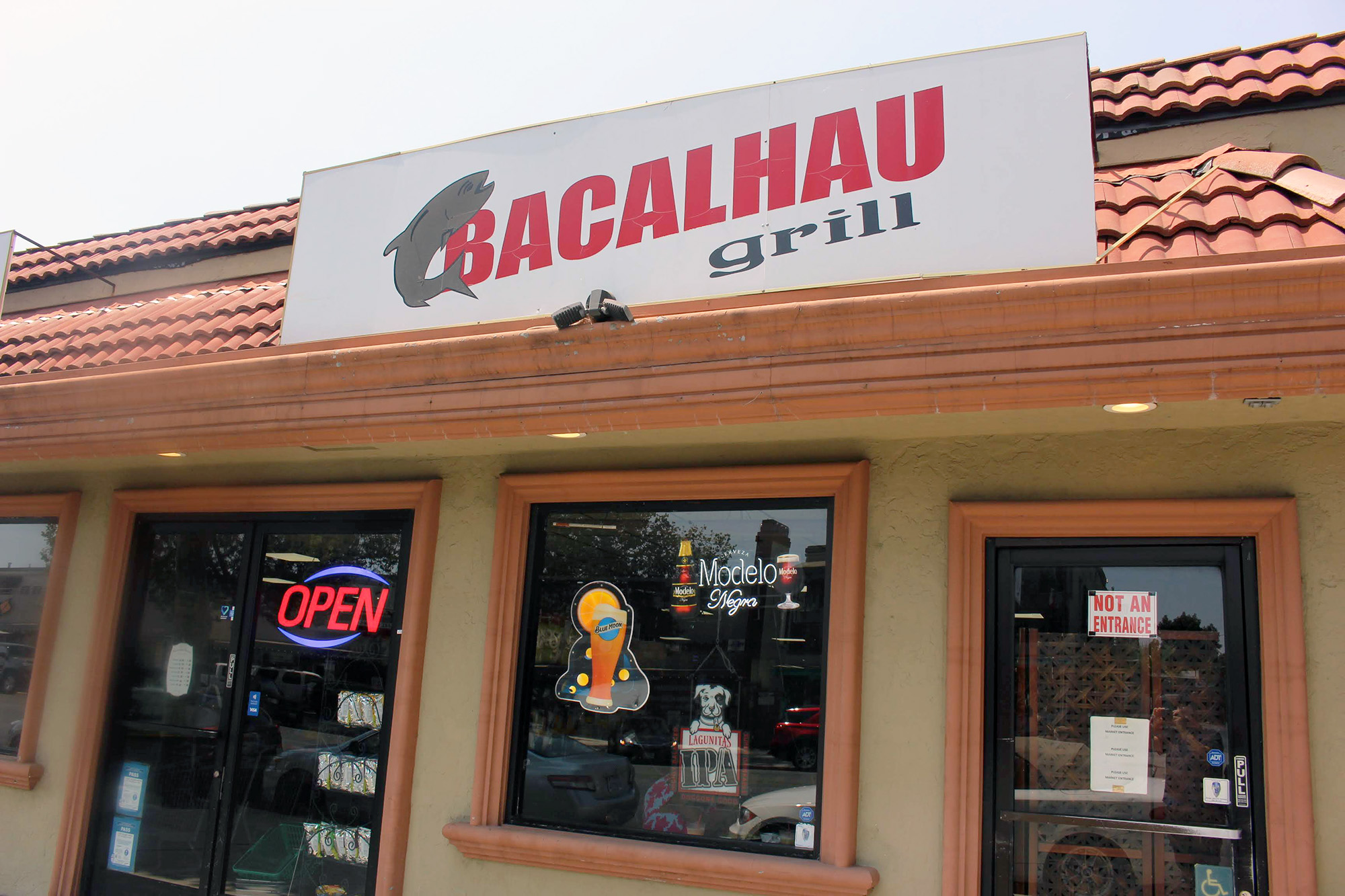 Exterior facade of a restaurant and market. The sign above reads "Bacalhau Grill."