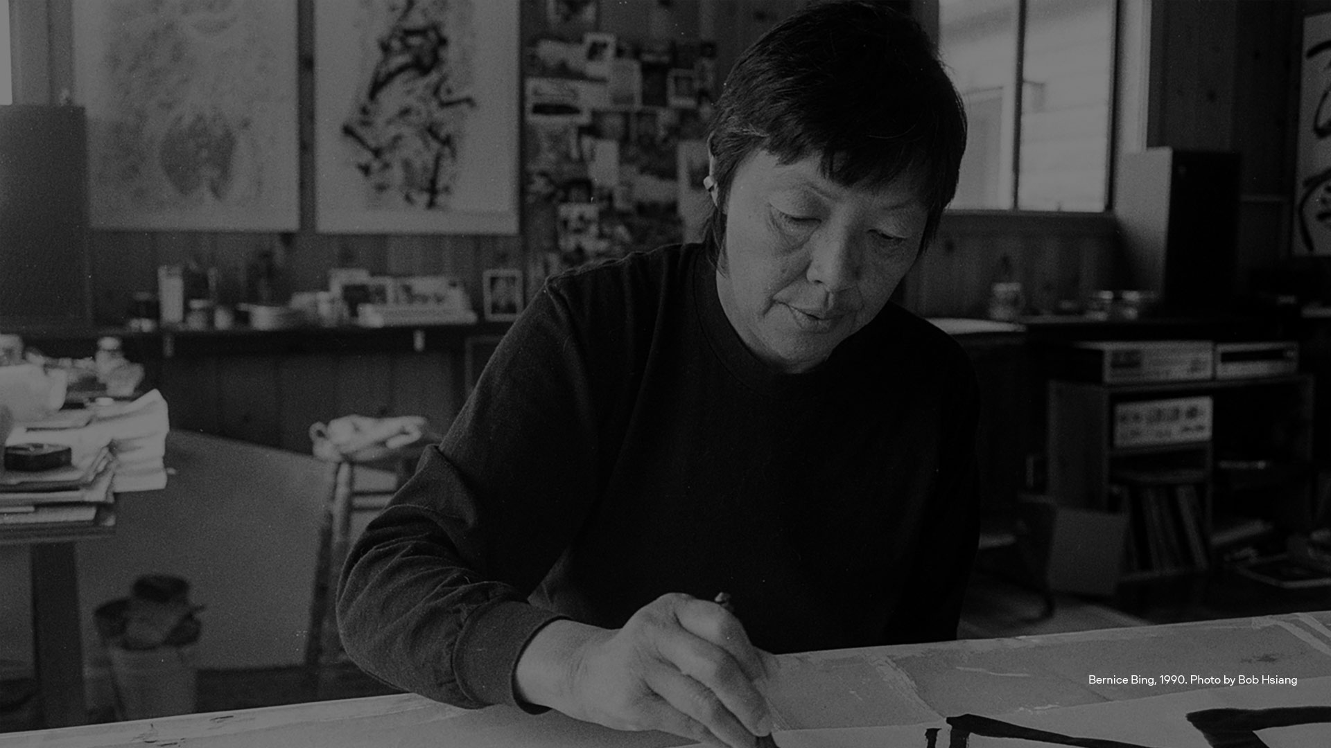 Older Asian woman artists at desk with pencil in right hand