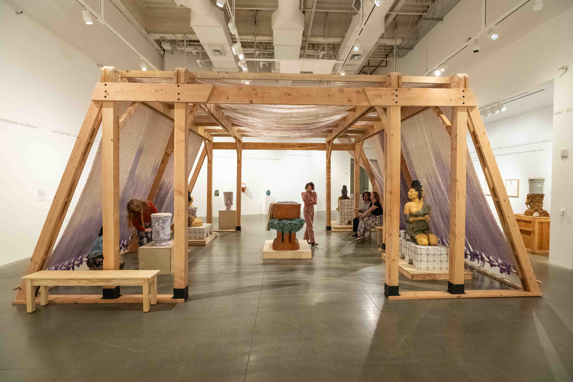 Wooden structure inside gallery space, draped with purple textile and surrounded by ceramic sculptures