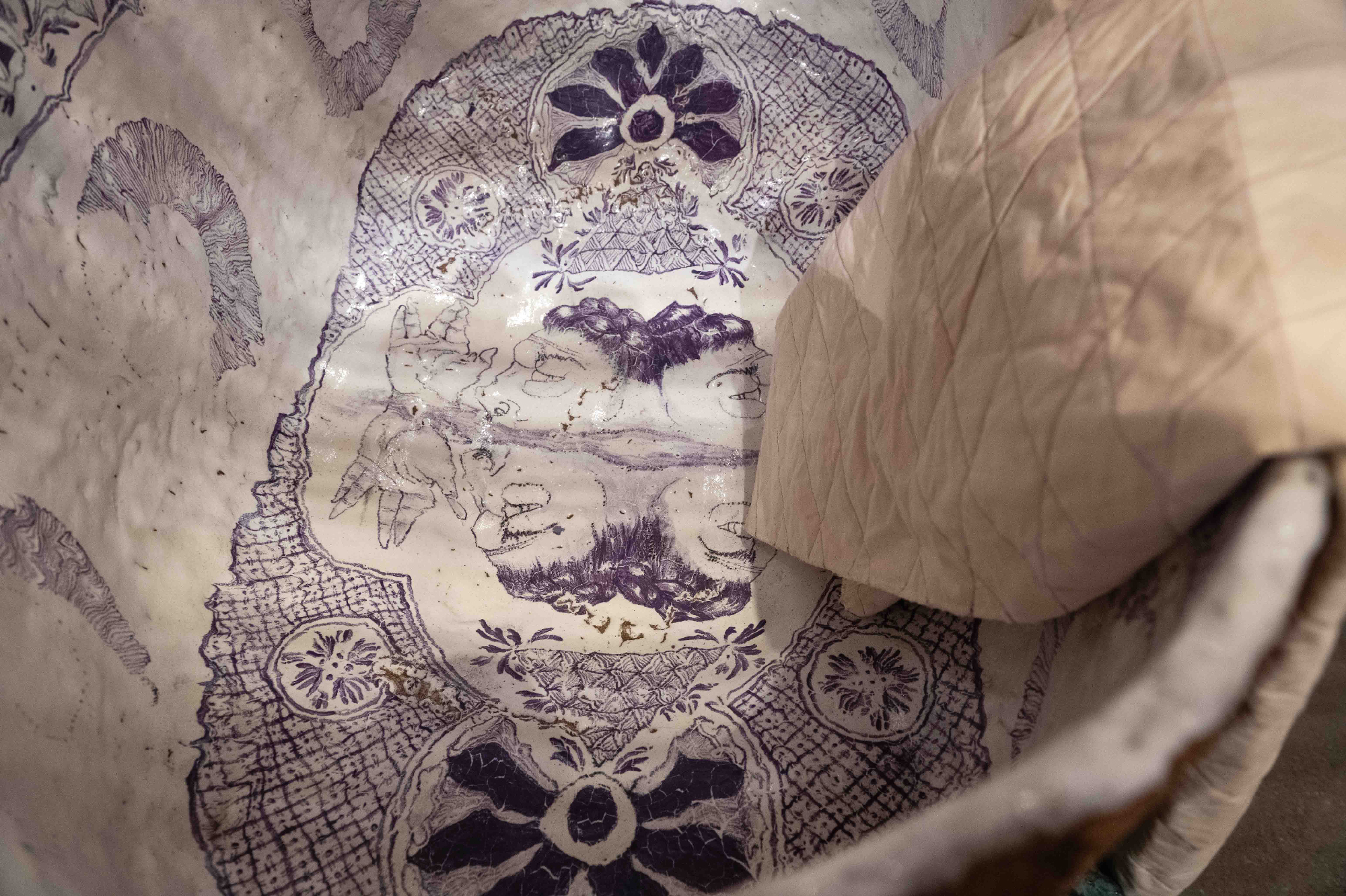 Delicate purple illustrations inside a glazed ceramic tub, fabric draped over side