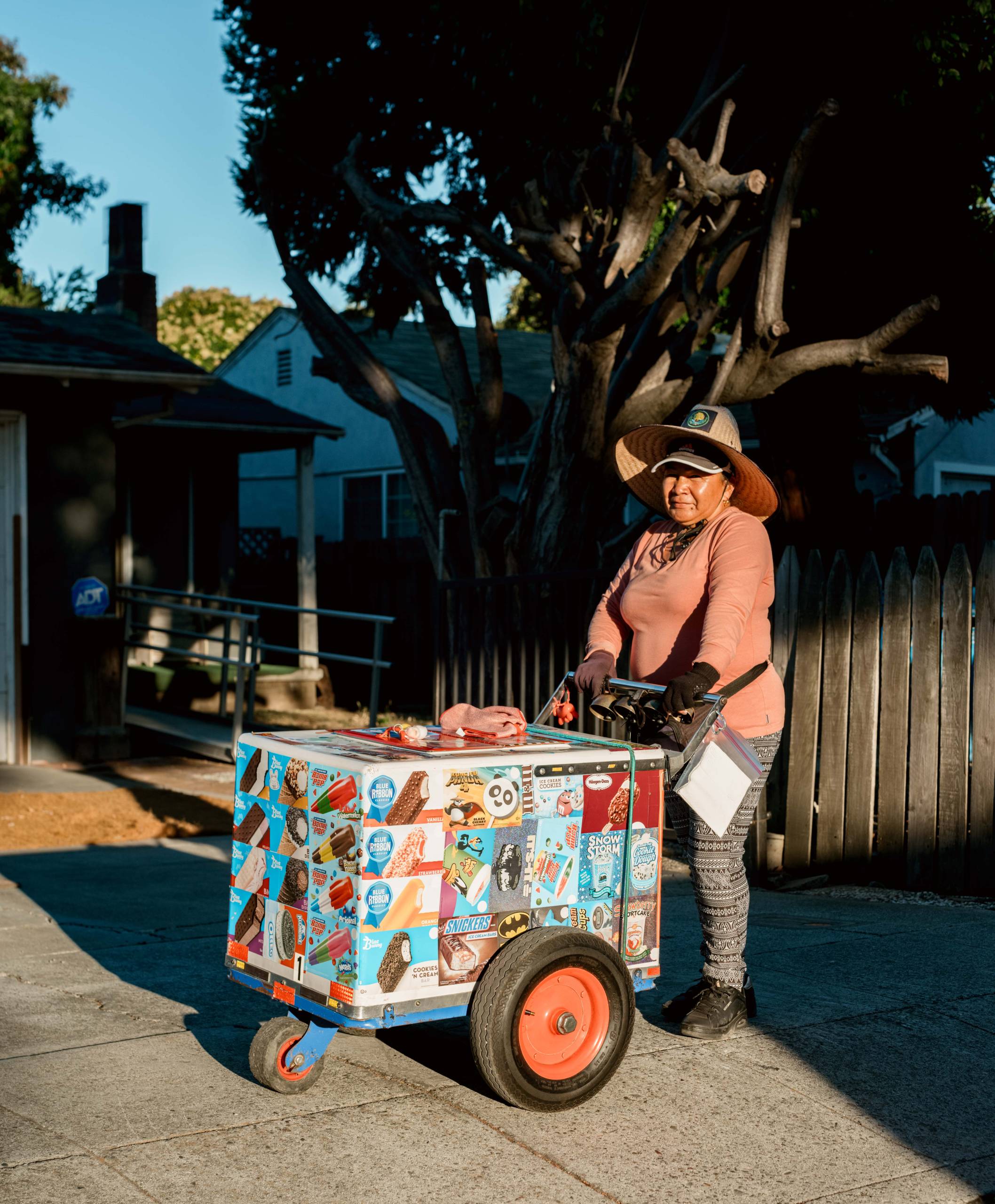 a Latina woman poses with her paleta cart in front of a driveway in East Palo Alto