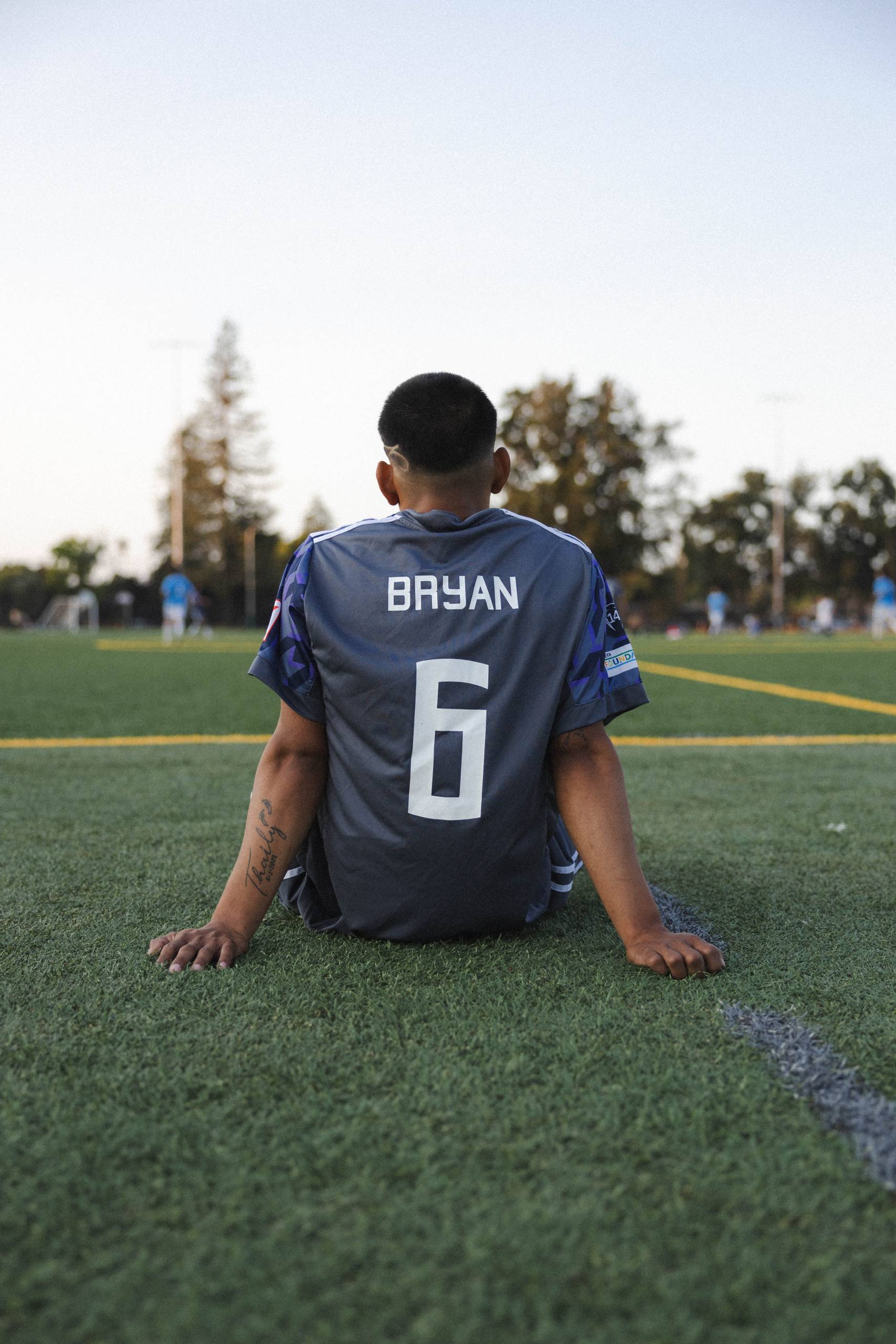 a soccer player rests on the sideline while his team plays on the field