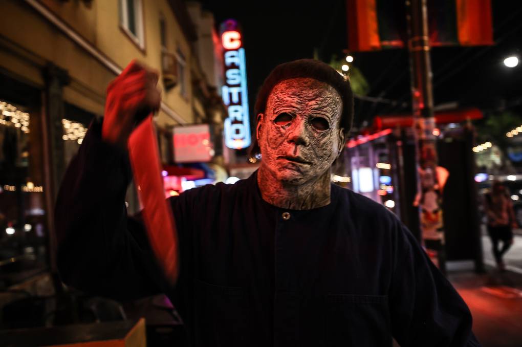 A man wearing a Michael Myers mask and boiler suit hold up a fake kitchen knife in the street.