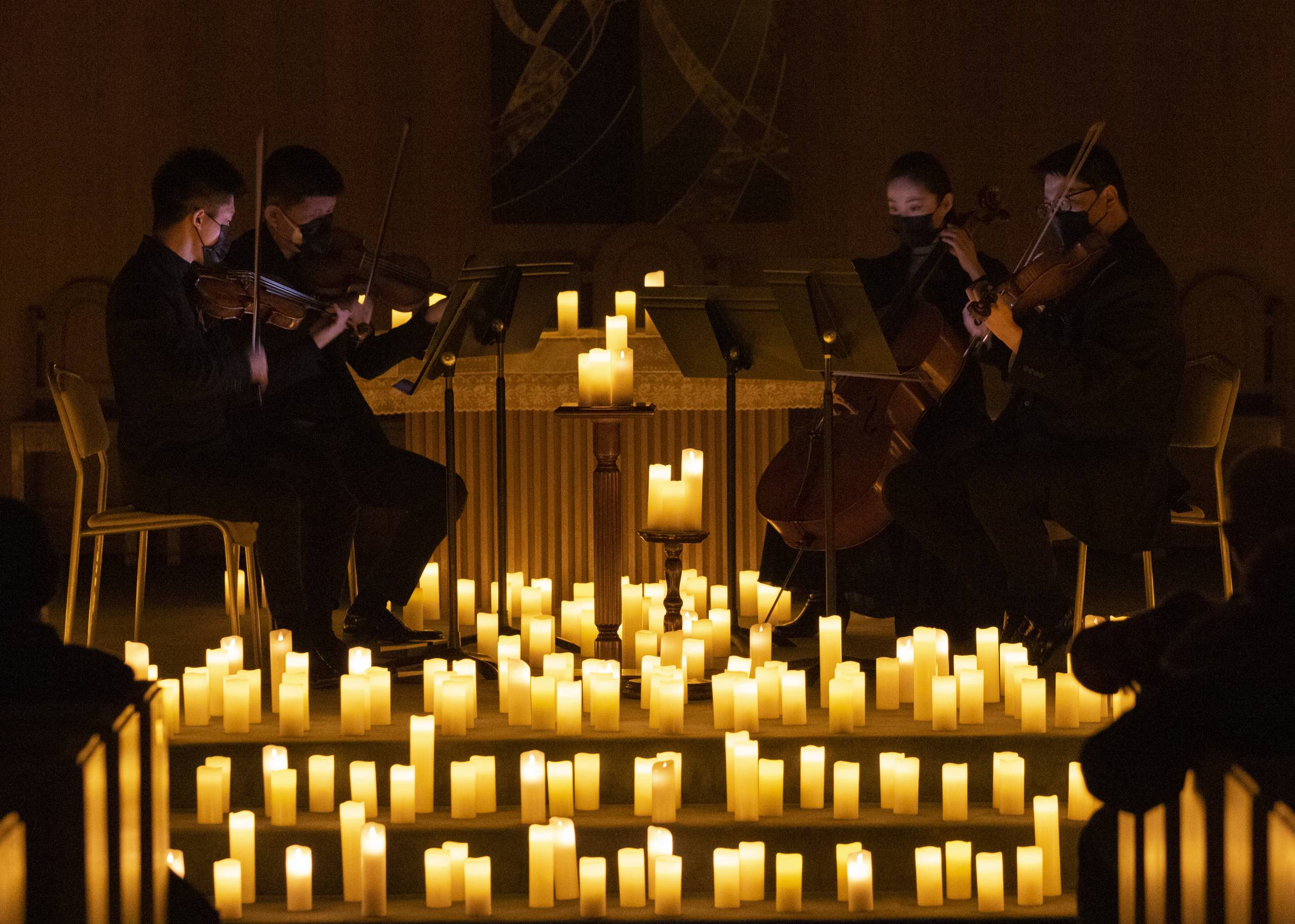 A string quartet performs in a circle, surrounded by candles.