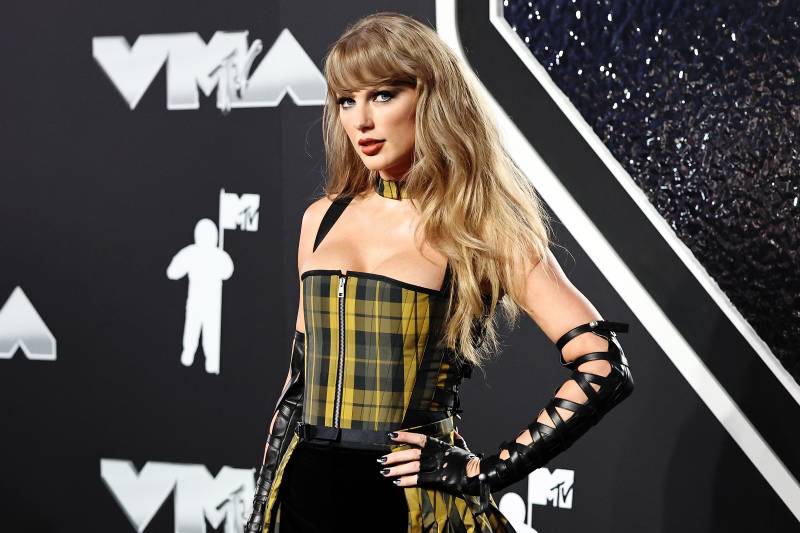 A glamorous woman wearing a plaid corset stands with hand on hip on a red carpet.