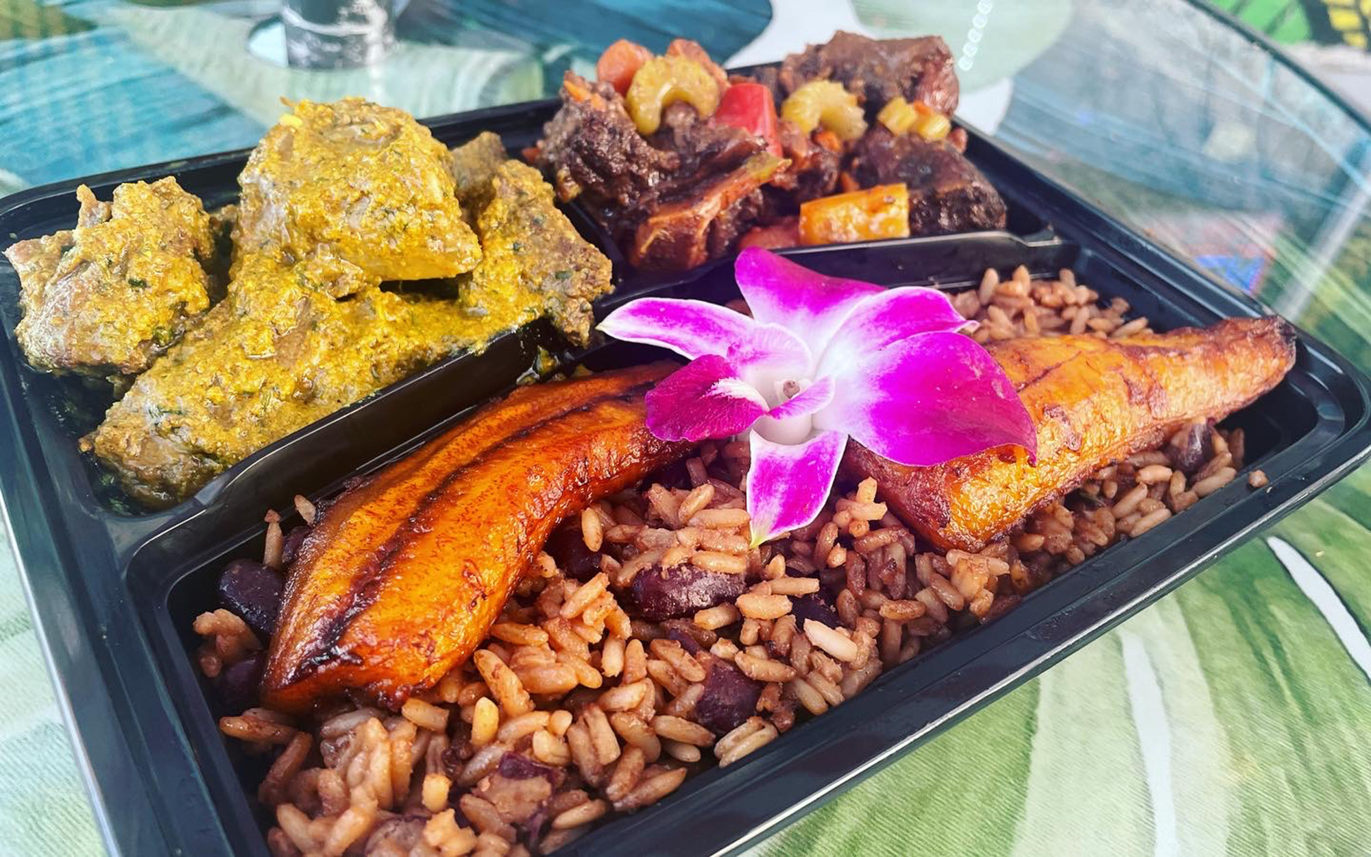 Takeout container with curry goat, braised oxtails, plantains, and rice and peas.