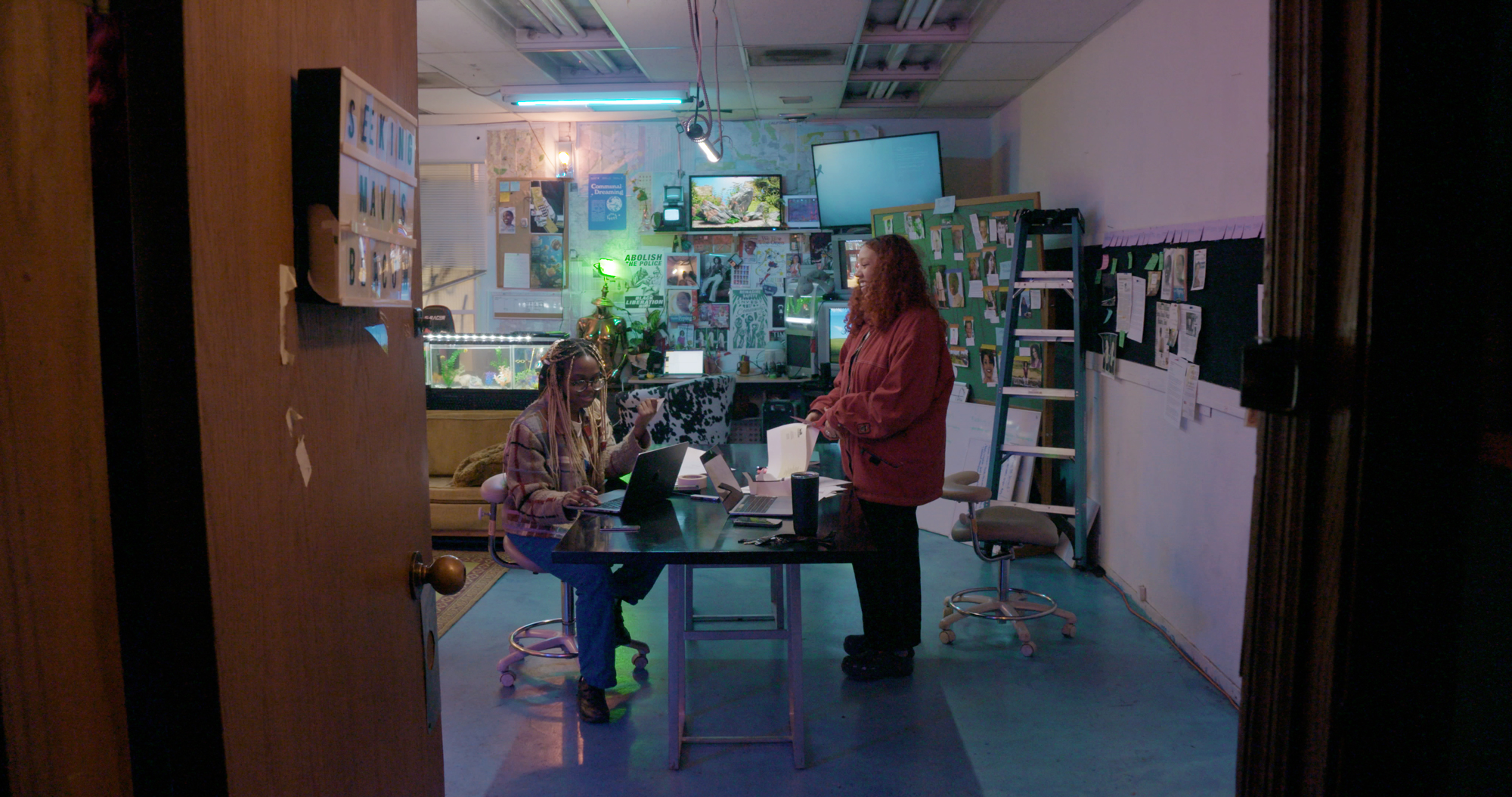 Two Black women face each other across table in eclectically decorated space