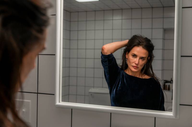 White woman with long dark hair looks in mirror