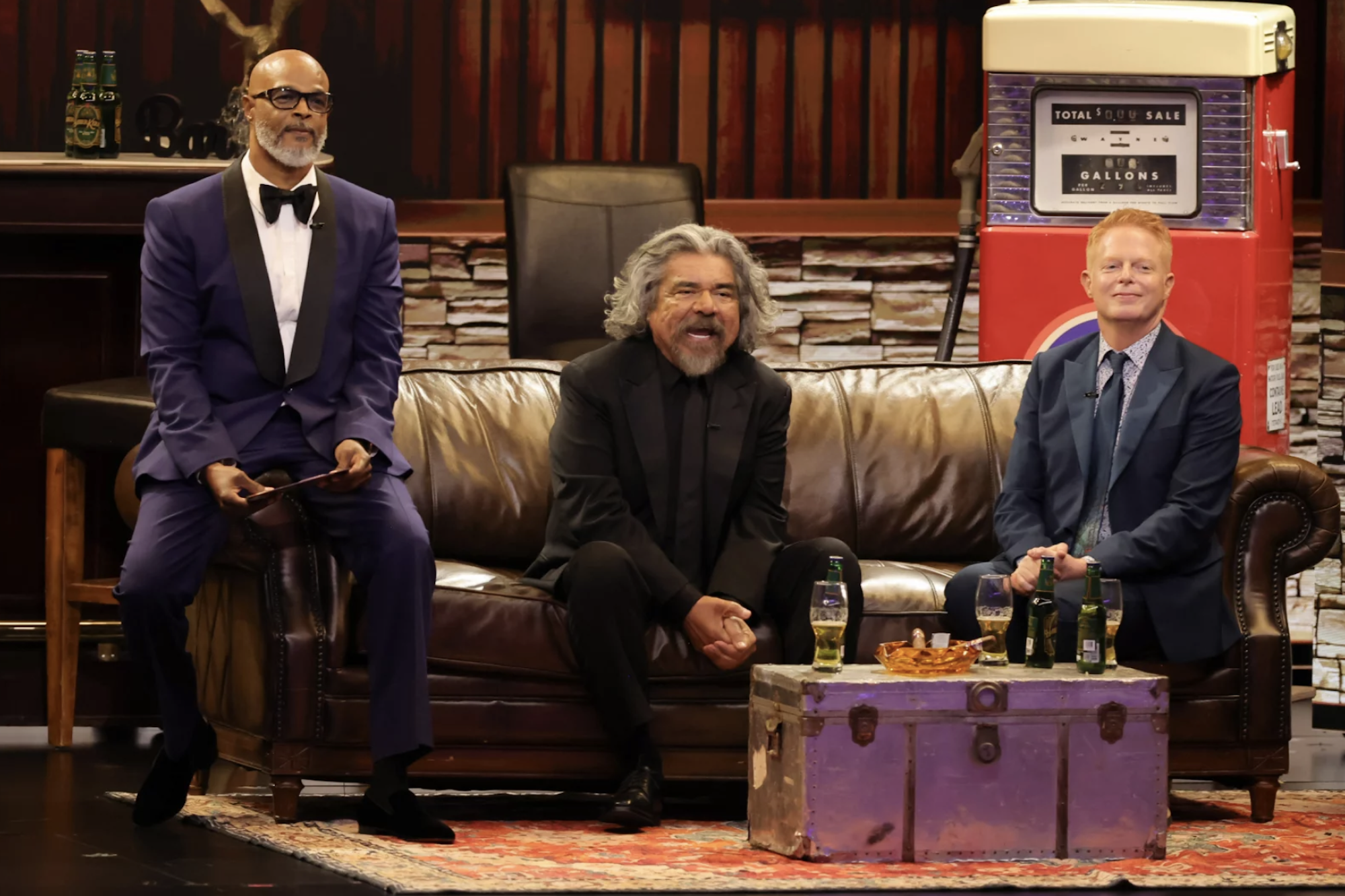 A Black man, a Latino man and a white man, all wearing nice suits, sit on a leather couch together.