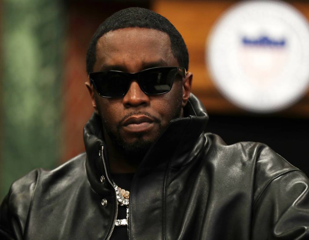 A black man wearing dark sunglasses and a black leather jacket with high collar.