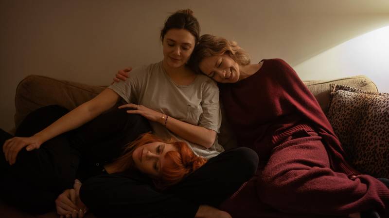 Three women sit on a couch, closely huddled together.