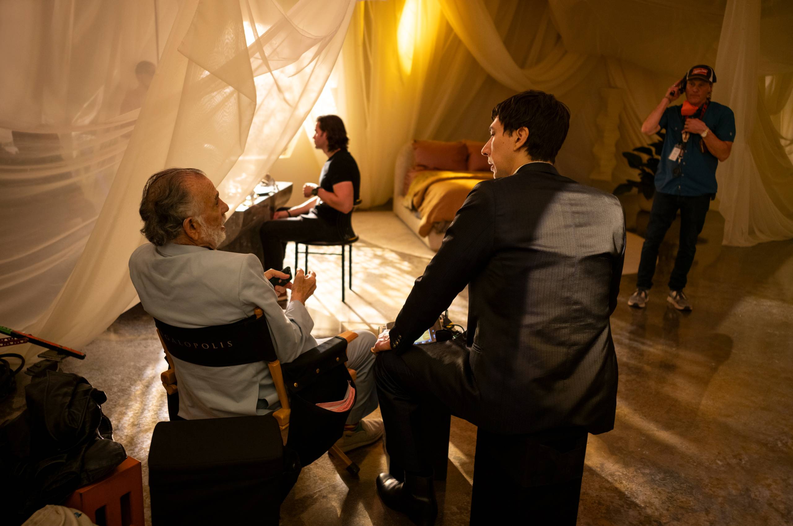 Older man talks to younger man, both seated on movie set