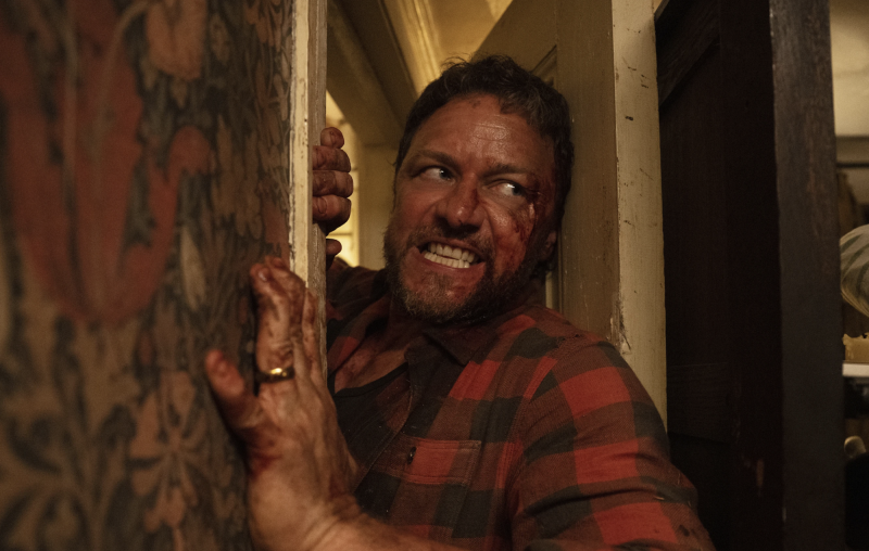 A bloodied, snarling man tries to force his way into a door.