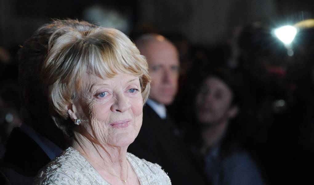 A senior woman smiles warmly on a red carpet.