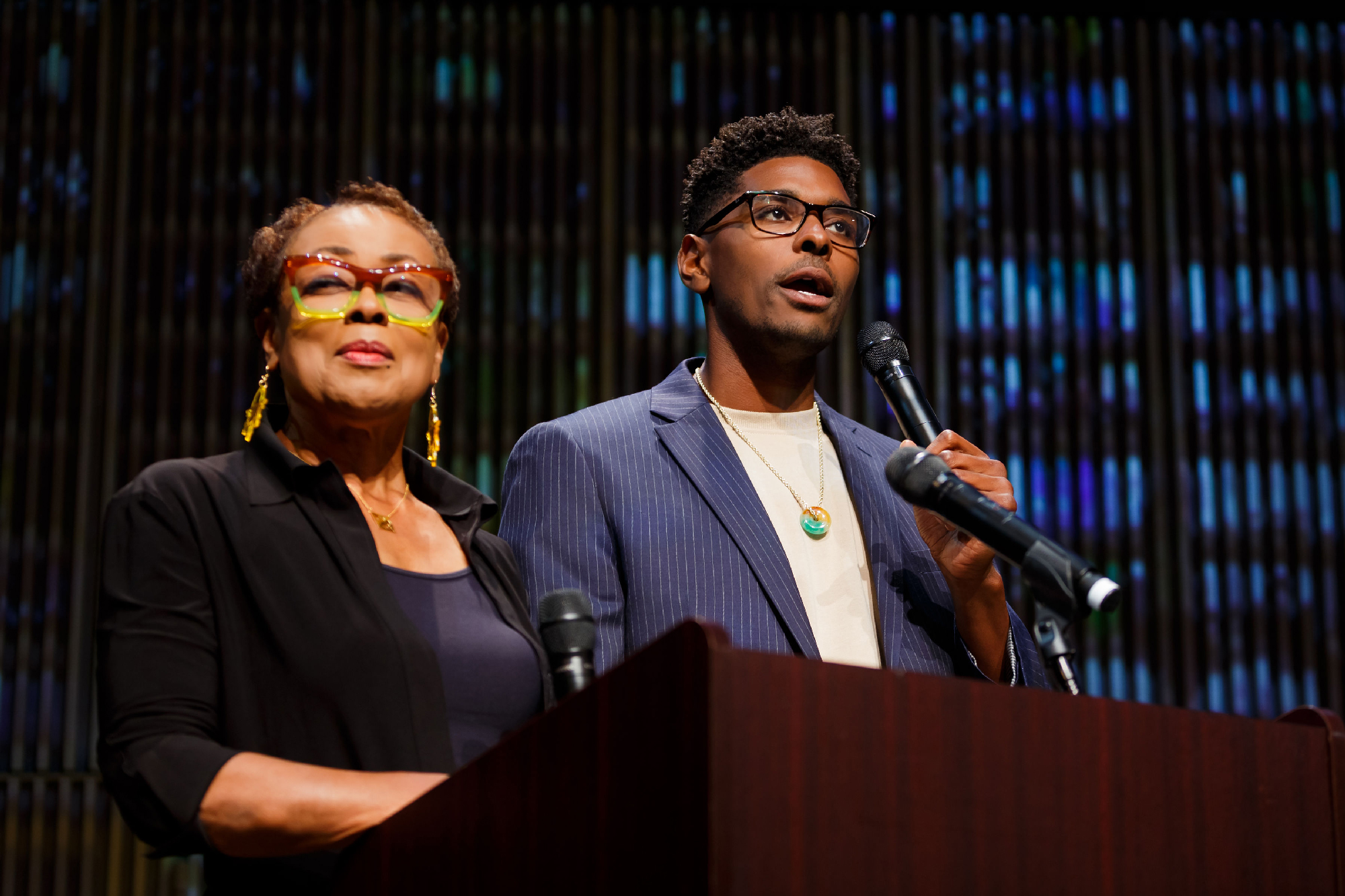 Black woman and Black man stand at podium with mics