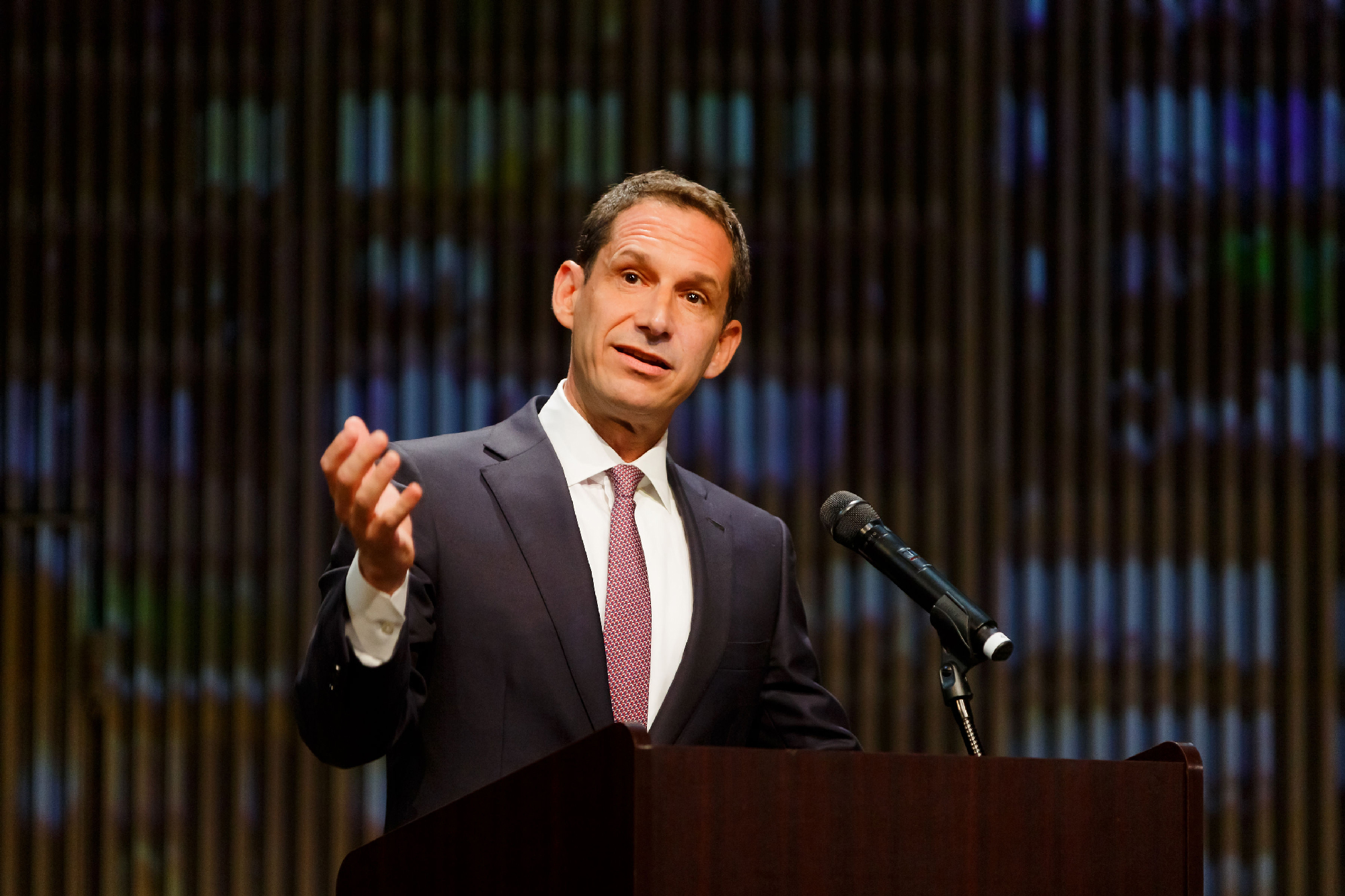 white man in suit gestures with one hand at podium