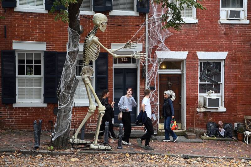 A 12-foot skeleton towers over four women on a street of red brick houses.