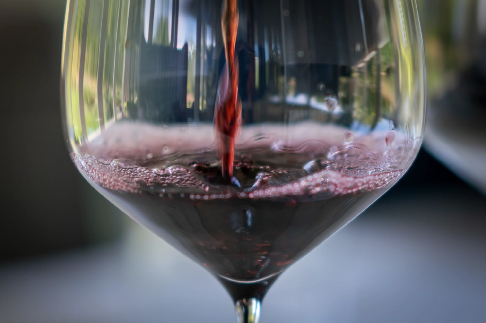 Red wine is poured into a clear wine glass.