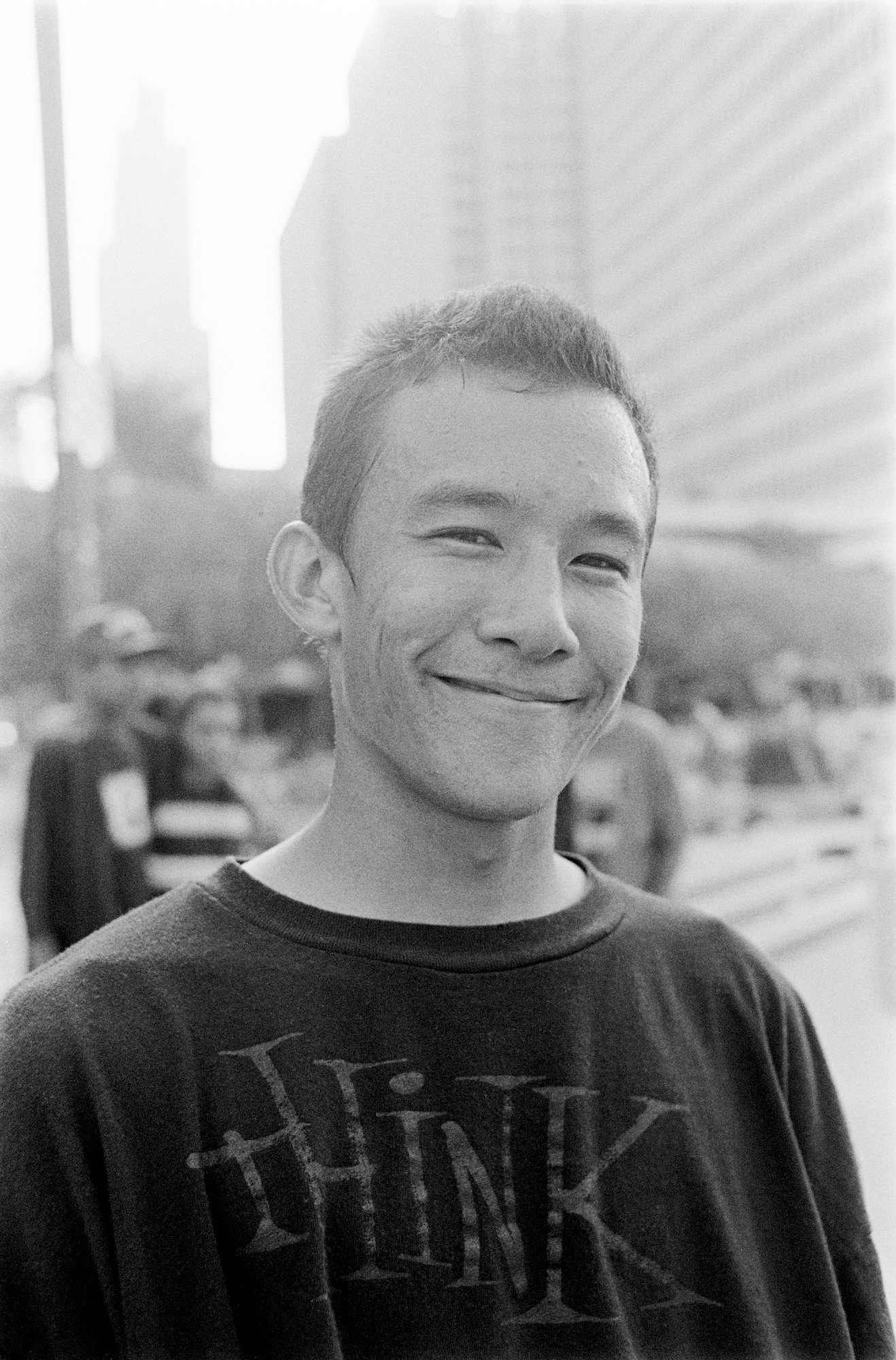 A young Asian man stands and smiles warmly for the camera in the middle of a city street.