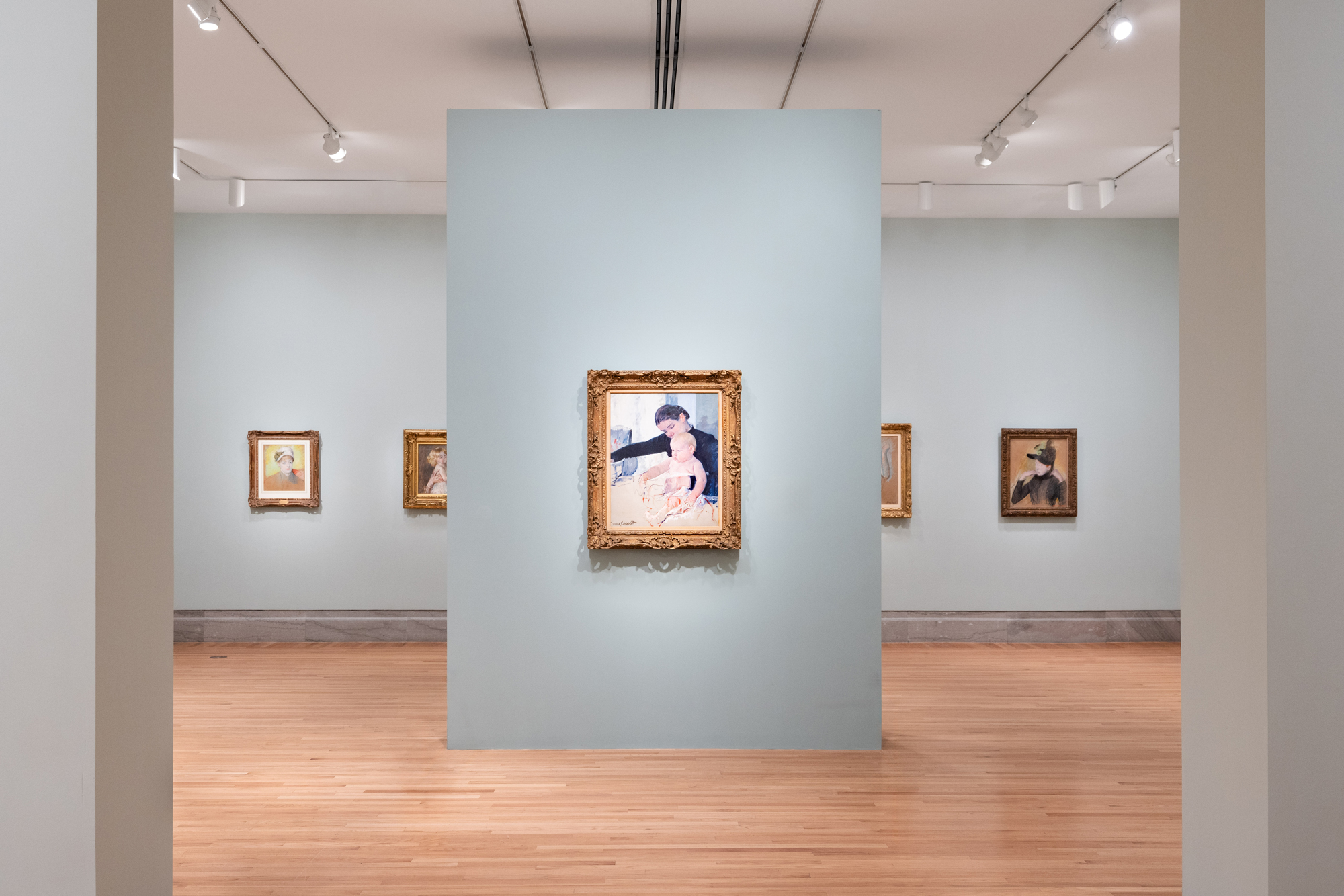 gray-walled gallery with framed paintings of women and children on walls