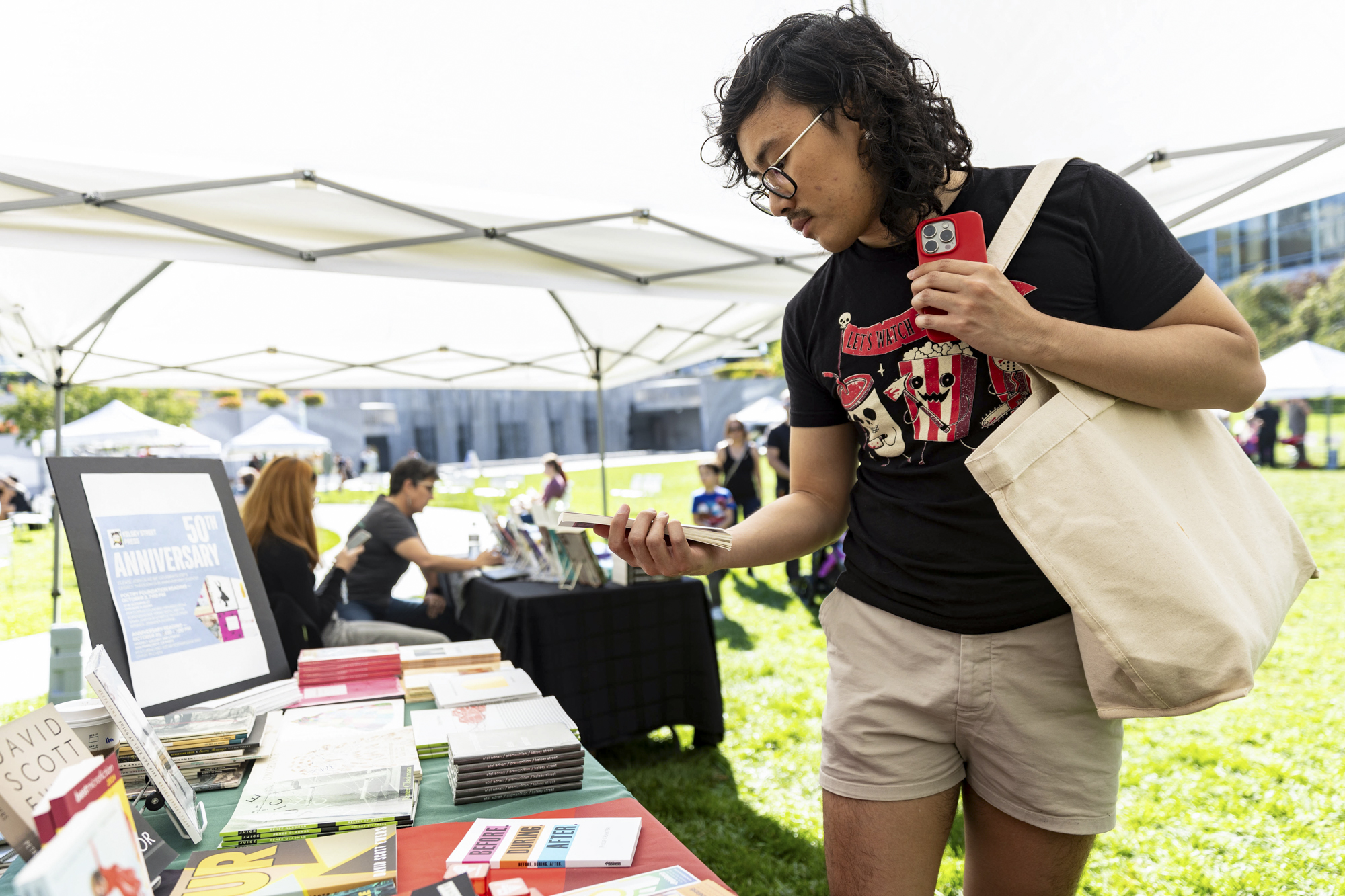 person looks at book picked up from table of books under tent at outdoor event