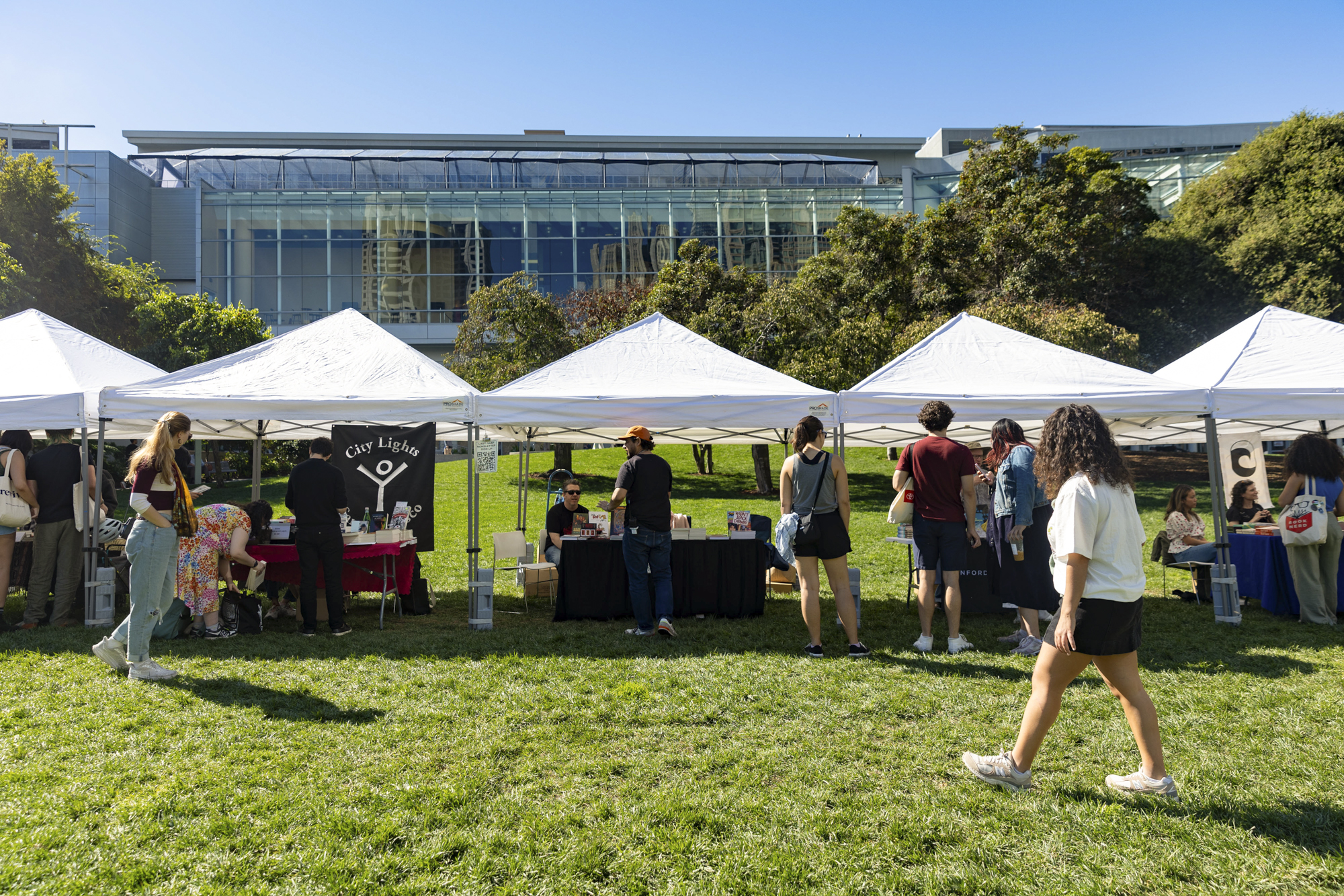 small crowd visit white tents on lawn with tables set up underneath