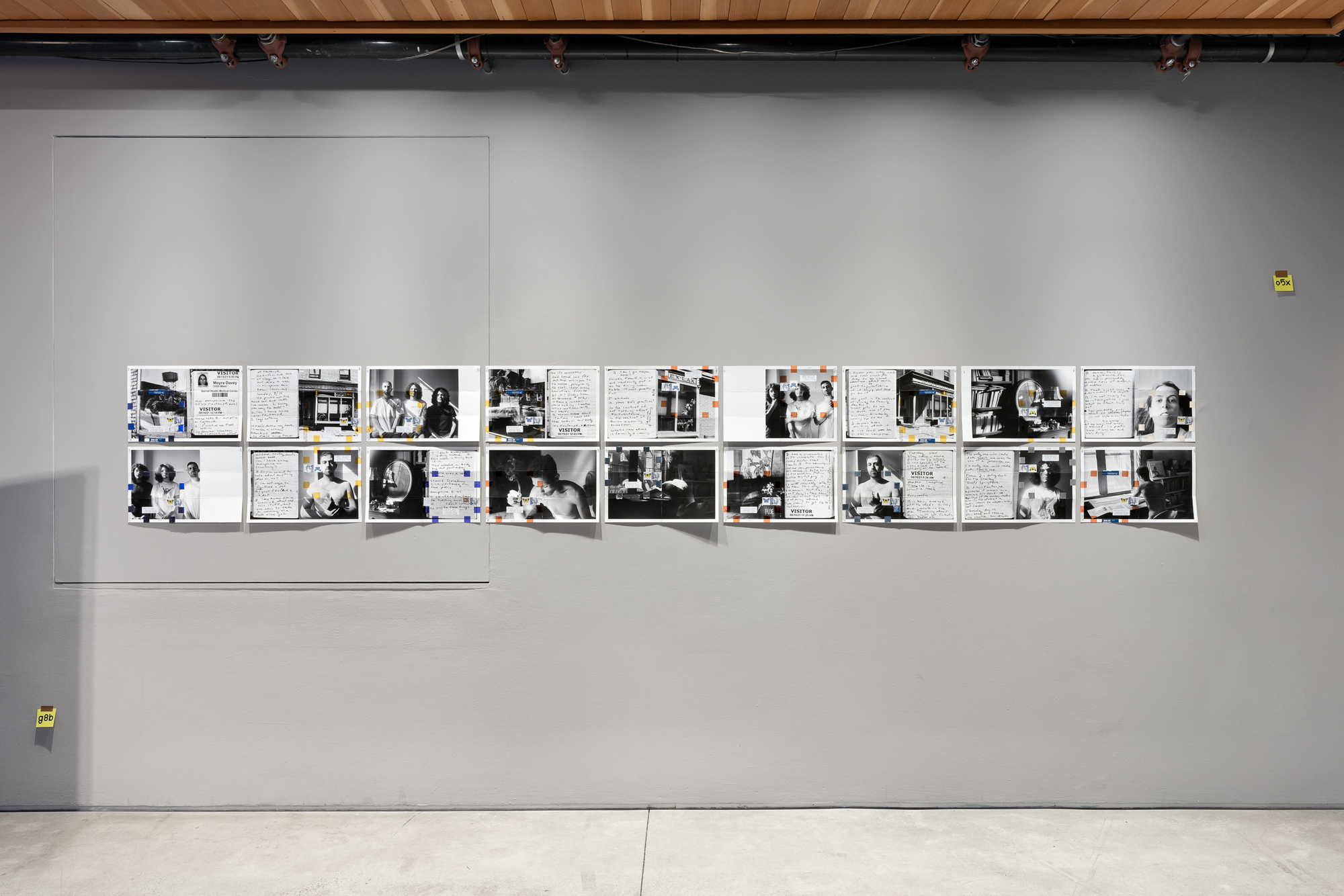 black-and-white photo prints folded and taped, in wide display on gray wall