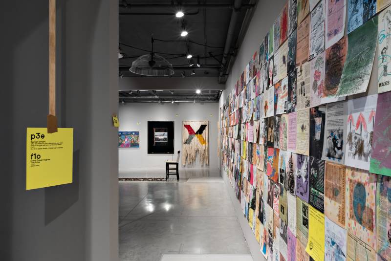 Gallery view with one long installation of multicolored paper, bright yellow paper hanging down from ceiling