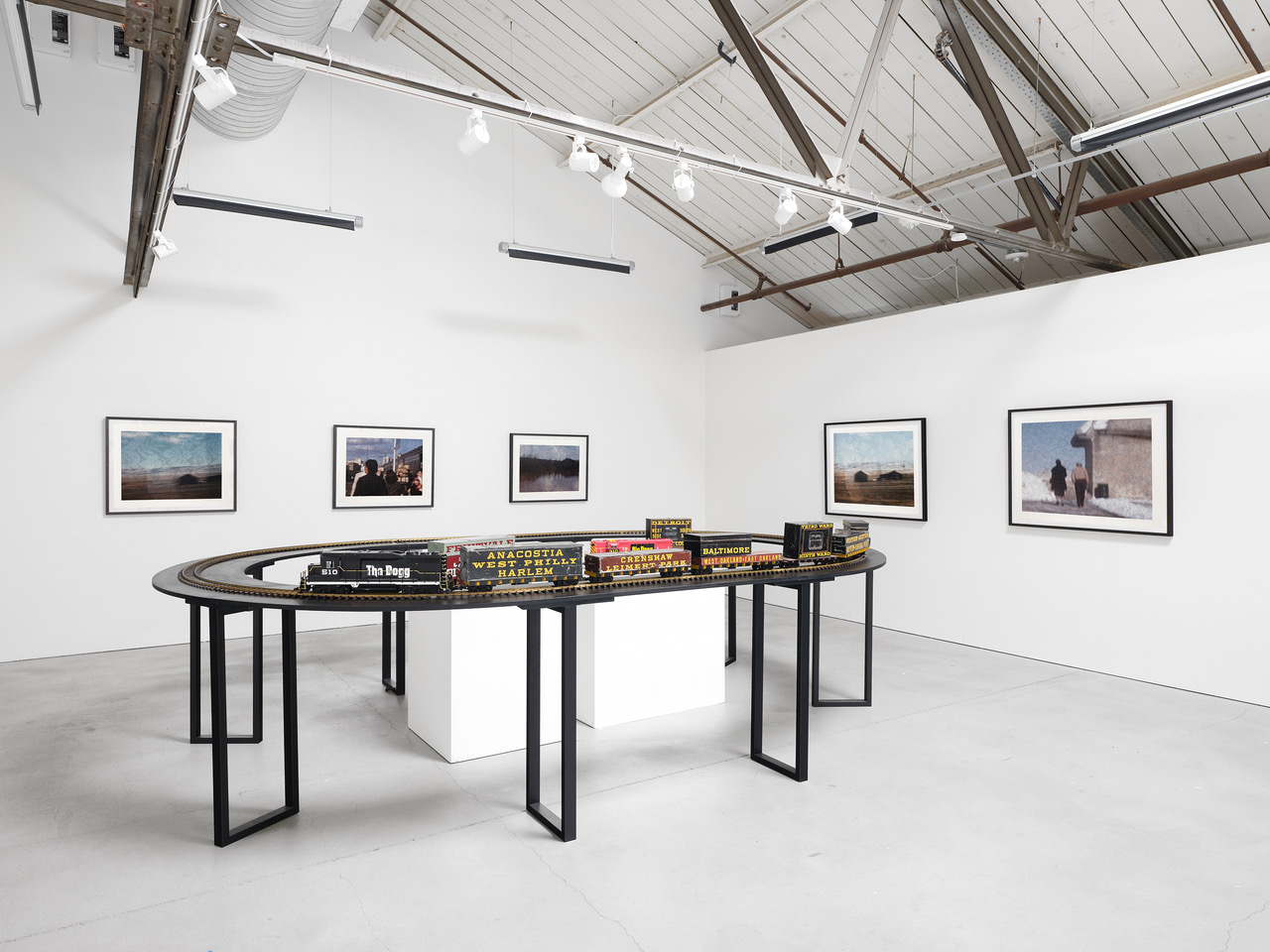 model train set up in white walled gallery with framed prints on walls