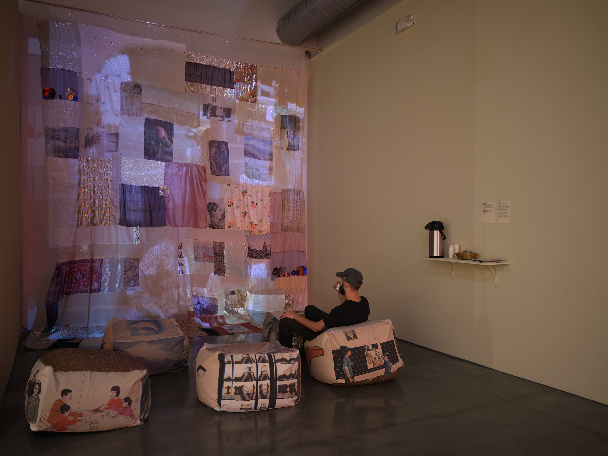 darkened corner with video projected on patchwork textile, beanbags and person sitting below